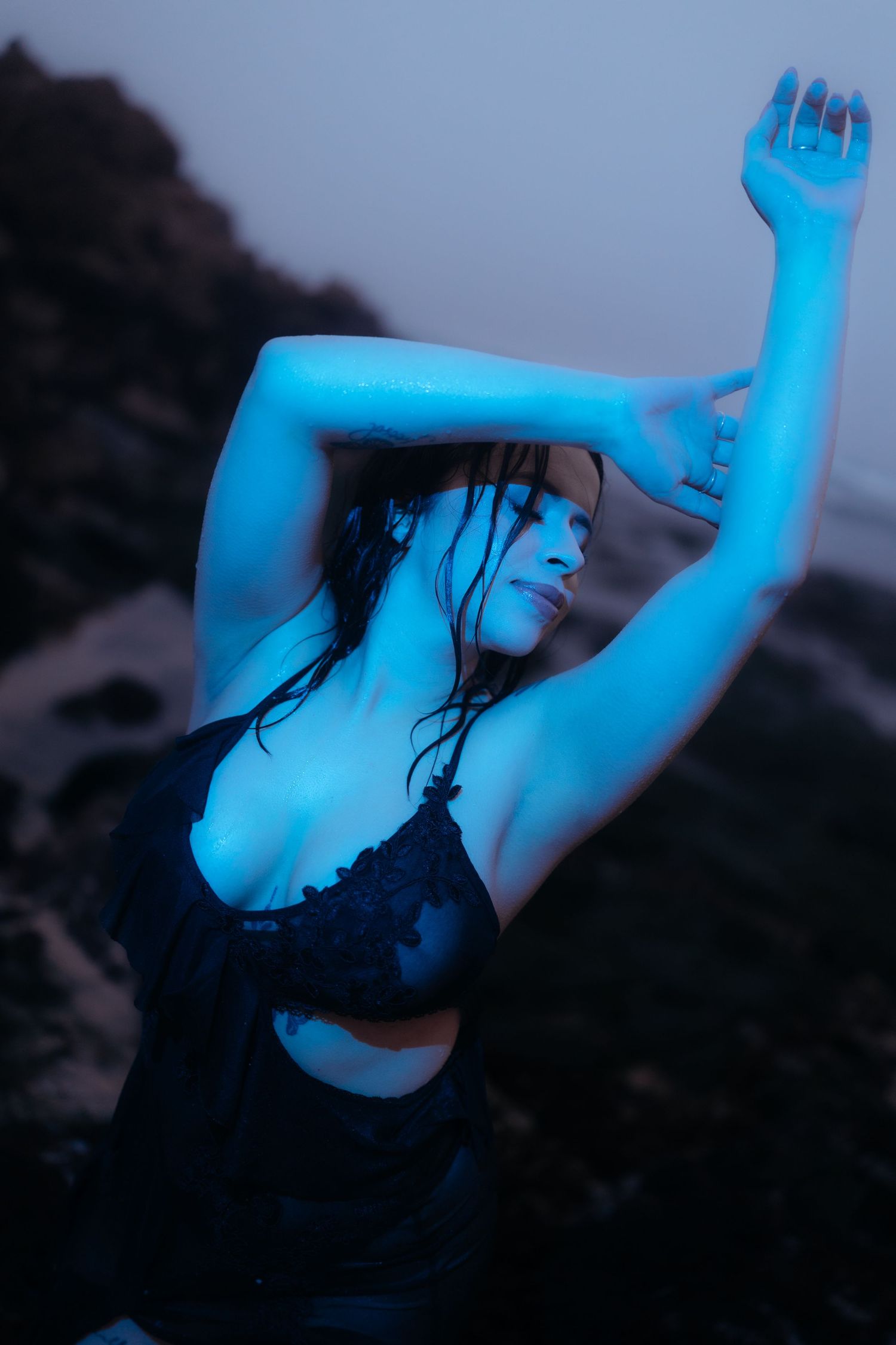 Dramatic blue-lit figure in black dress dancing on beach at twilight.