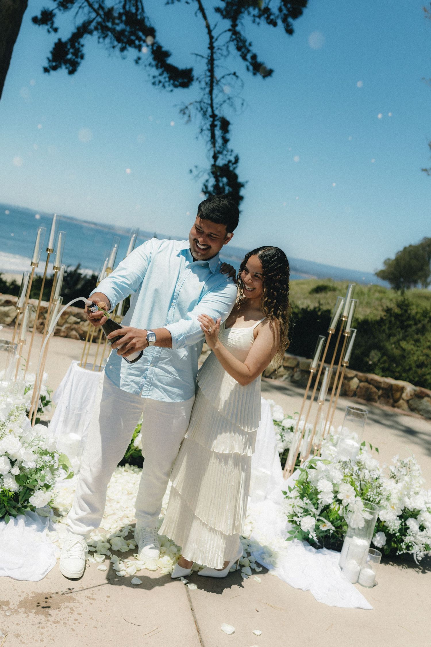 Couple in white attire celebrating at an outdoor beach wedding ceremony with floral arrangements.