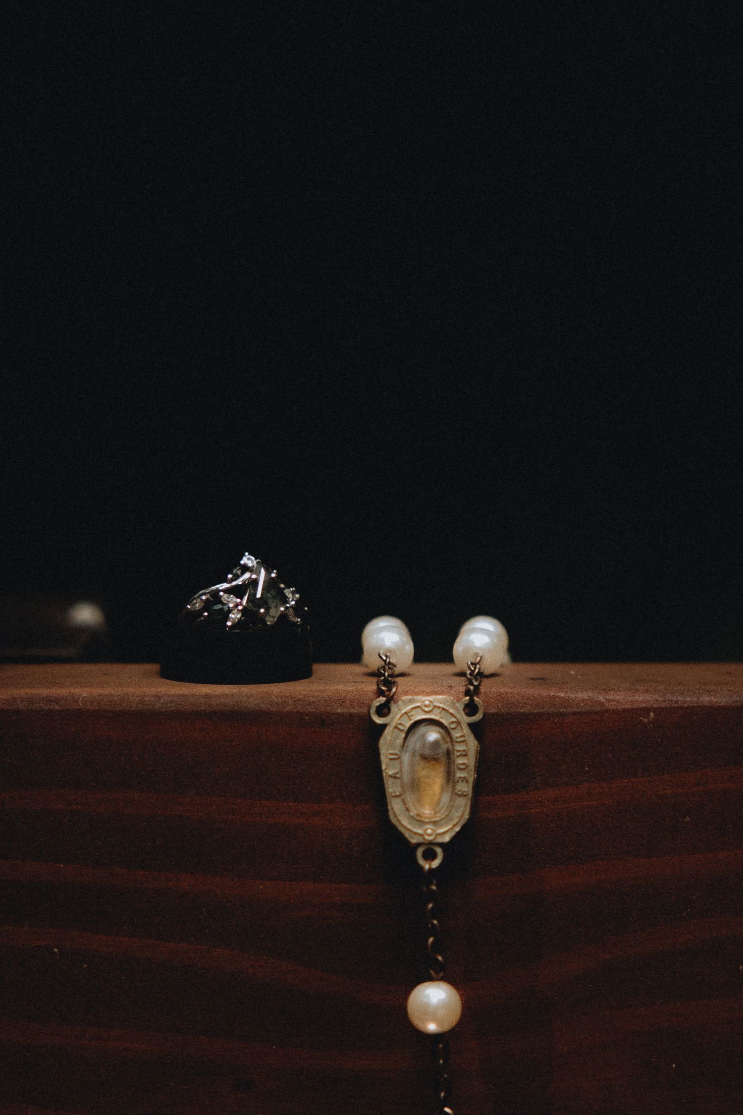 Pearl and brass jewelry components arranged in a minimalist sequence on dark wood surface showing progressive assembly.