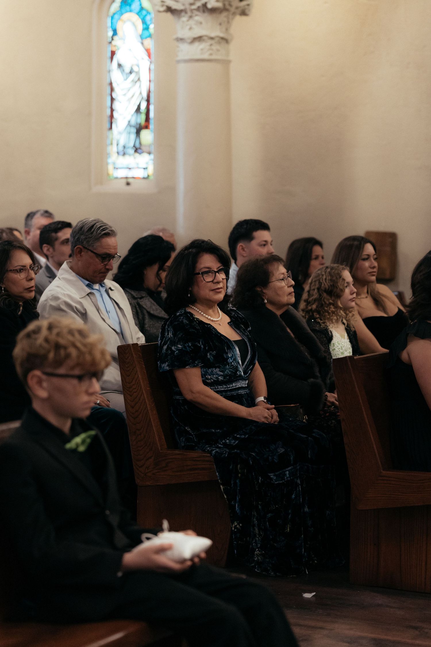 Wedding guests seated in wooden pews inside a church during a ceremony.