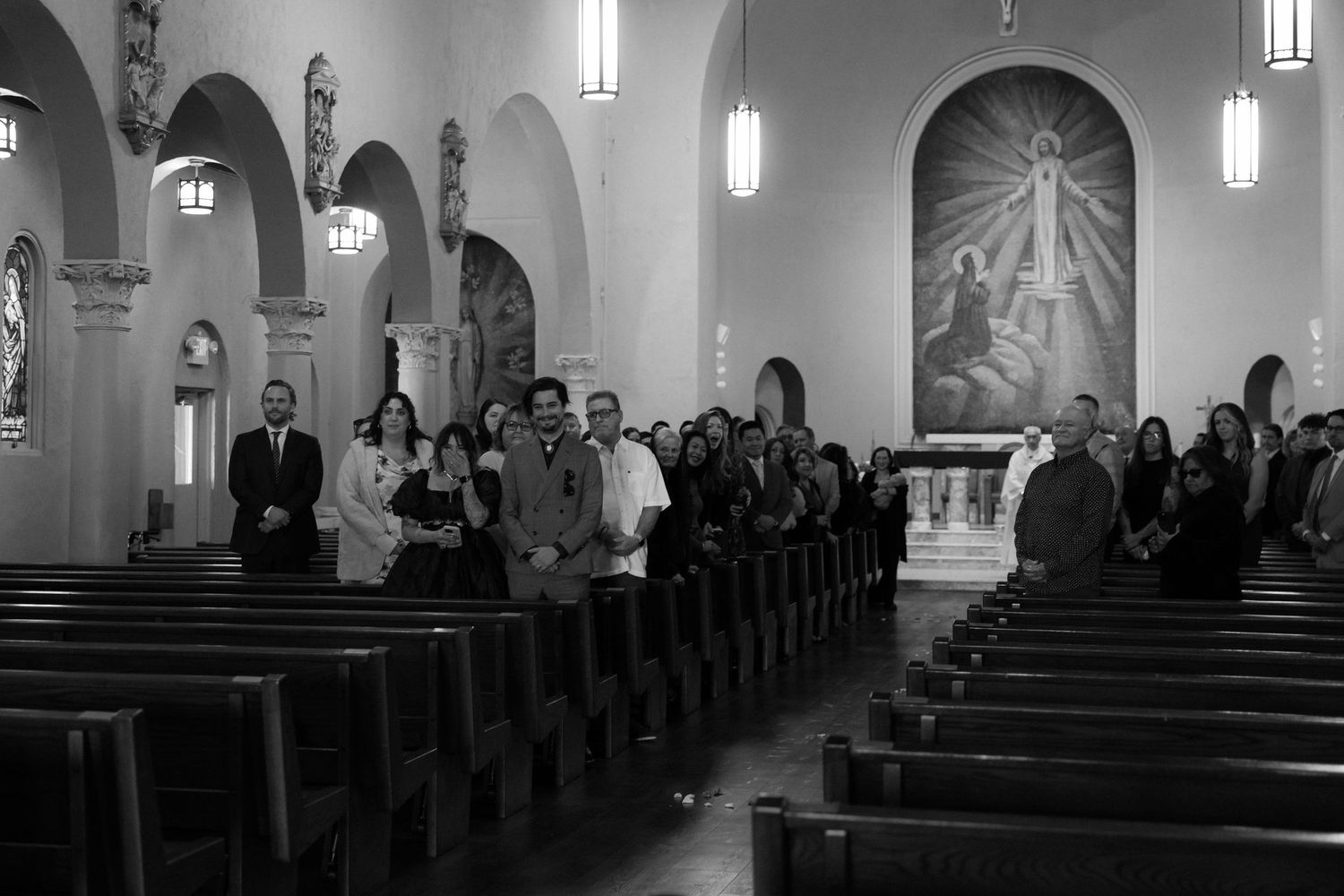 Wedding ceremony guests seated in church pews during traditional service in elegant chapel with arched ceilings.