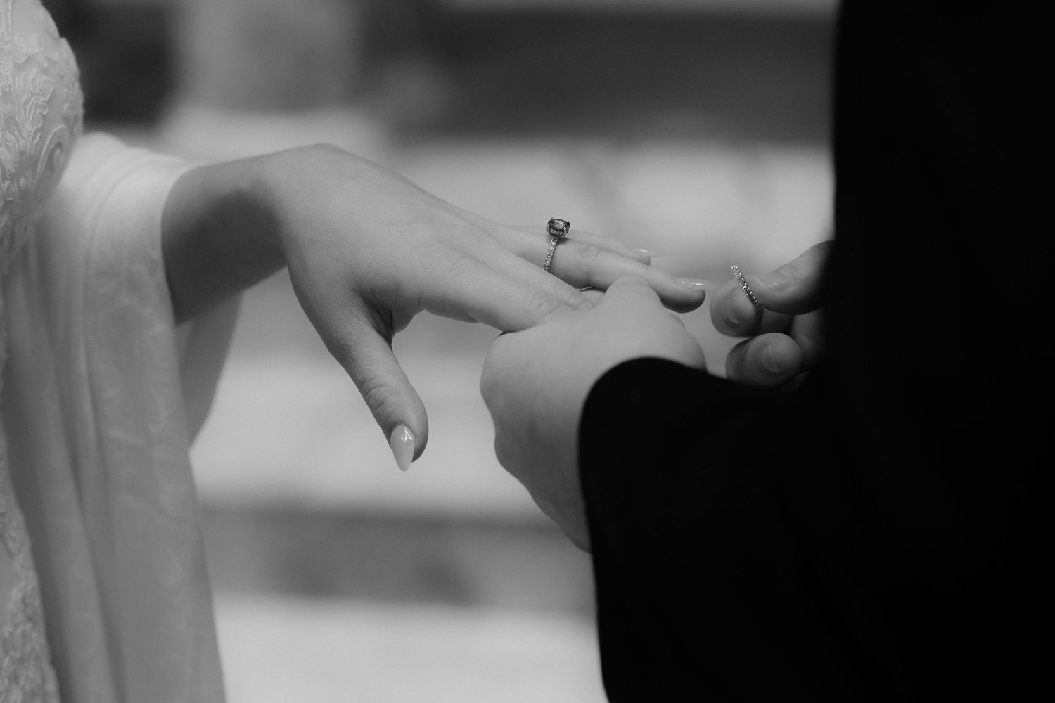 A black and white close-up of hands exchanging rings during a wedding ceremony.
