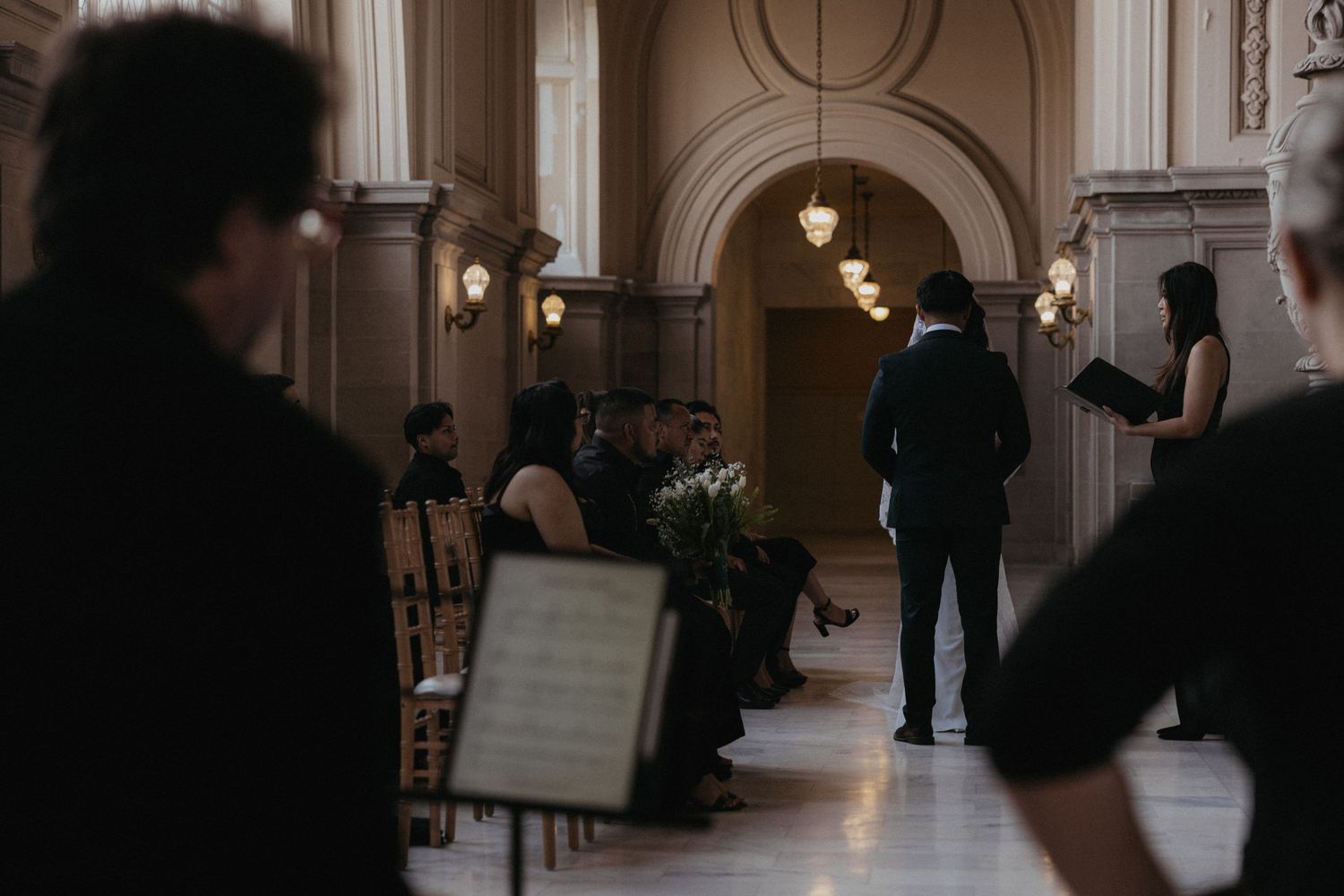 Wedding ceremony preparations in a dimly lit classical hallway with pendant lighting.