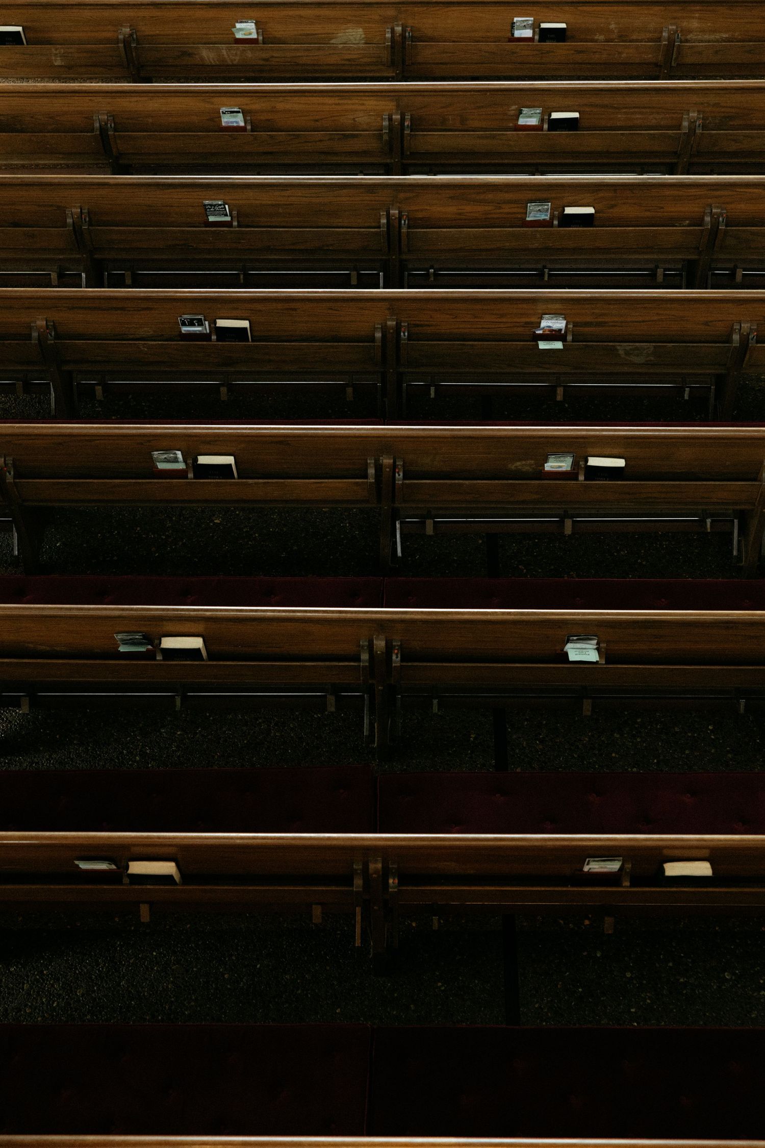 Empty wooden church pews arranged in rows, with small hymnal holders attached to the backs.