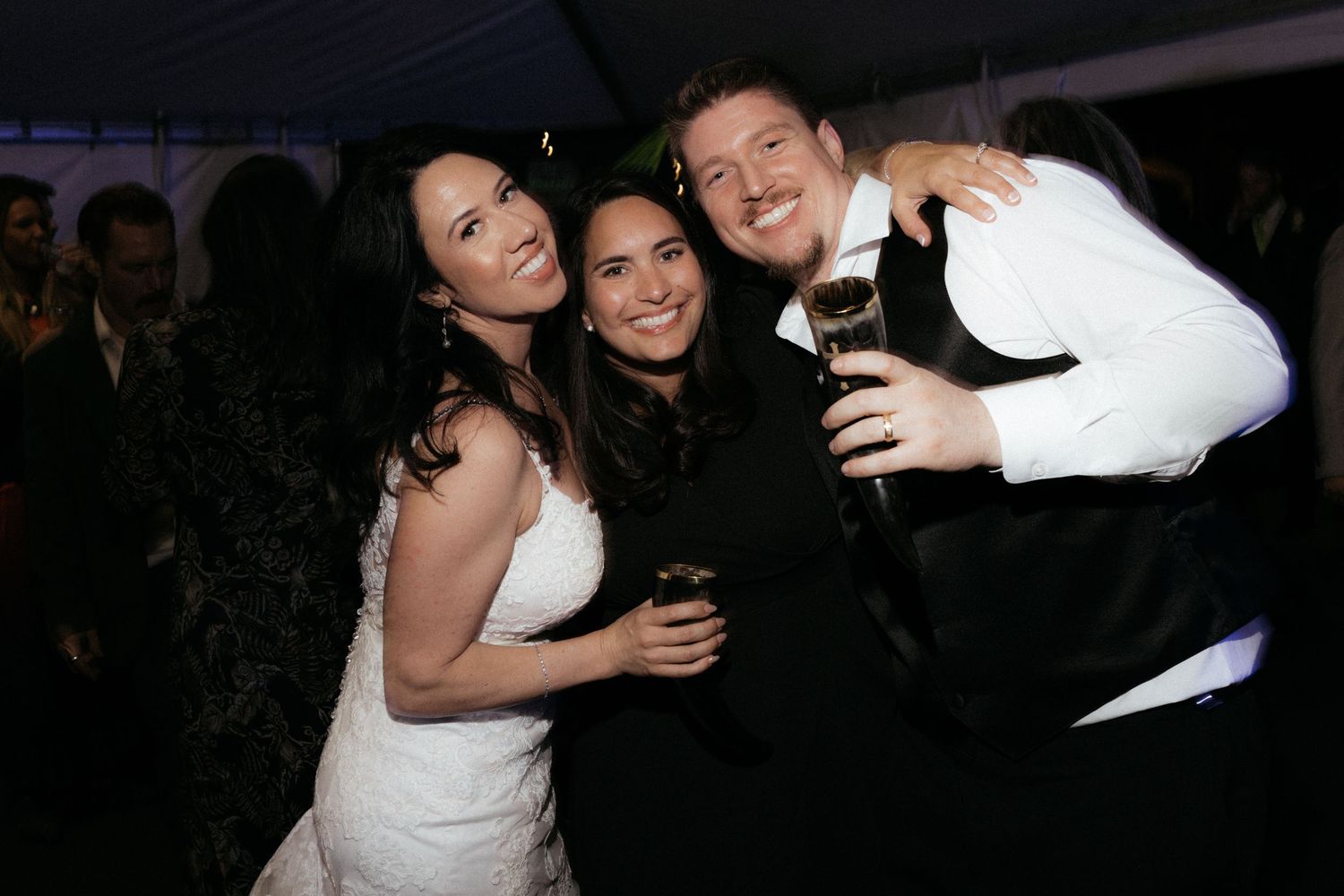 Wedding party members embrace and laugh during an evening celebration.
