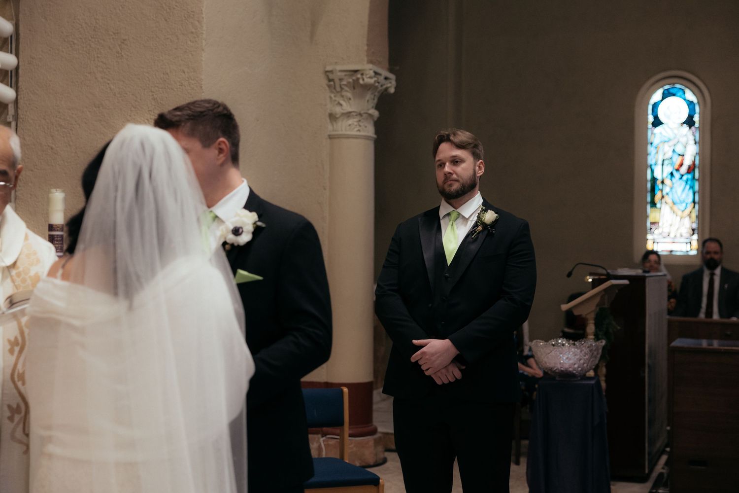 A wedding ceremony unfolds in a church sanctuary with ornate religious artwork on the walls.