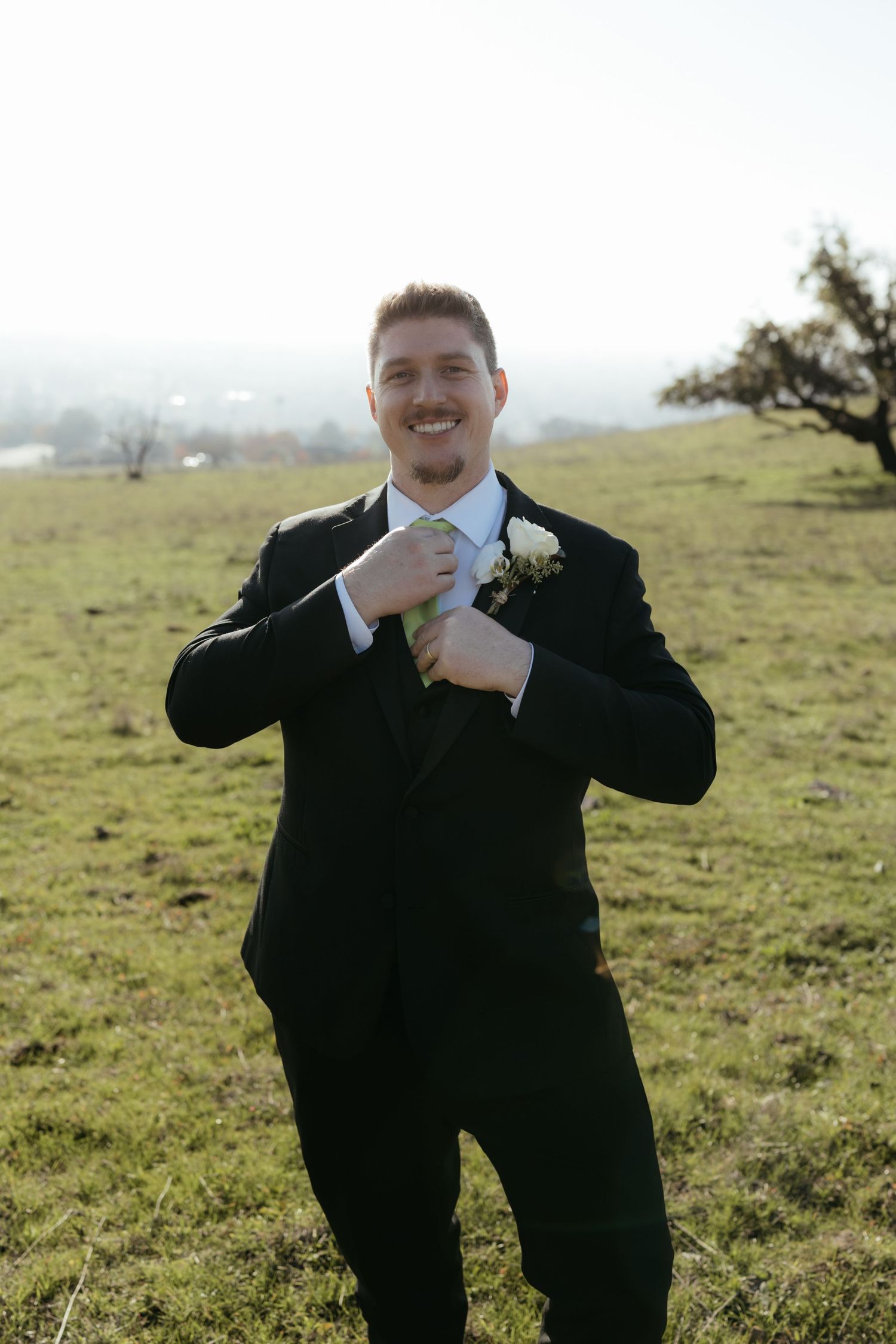 Groomsmen in black suits pose playfully in a sunny field.