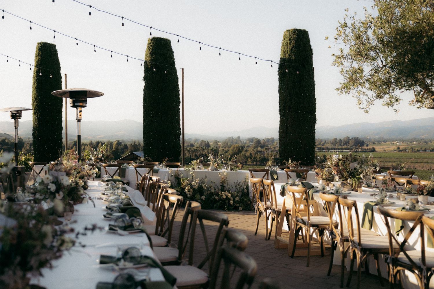 Elegant outdoor restaurant terrace with panoramic views of rolling hills and cypress trees in Tuscany at sunset.