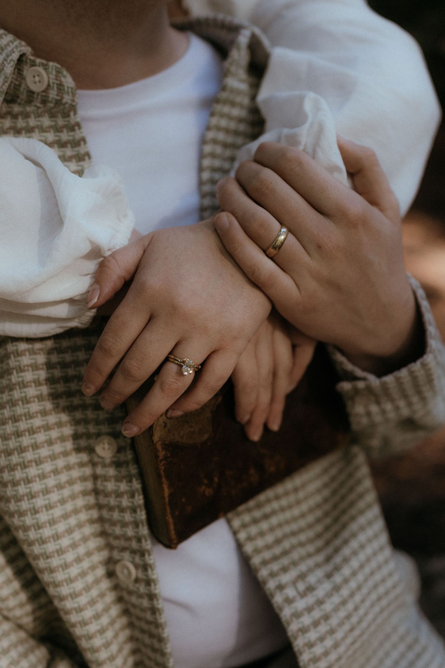 Close-up of hands wearing engagement rings with a vintage book and plaid fabric in the background.