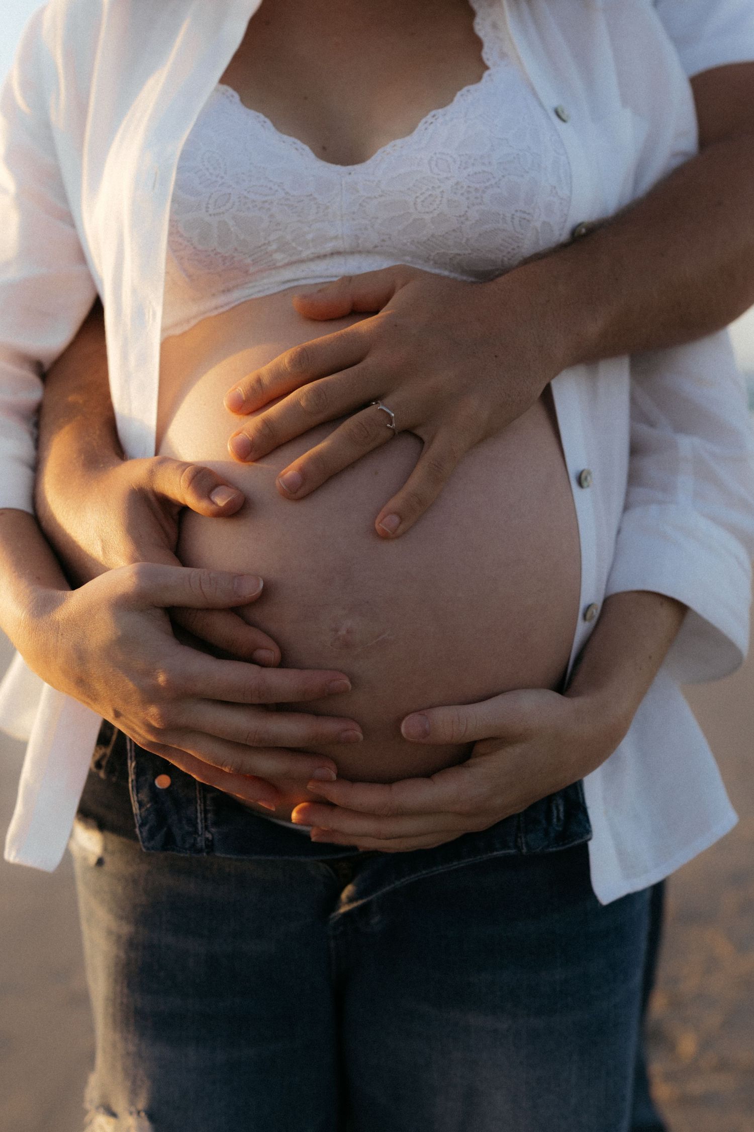 Close-up series of hands gently resting on stomach in white shirt and jeans during golden hour.