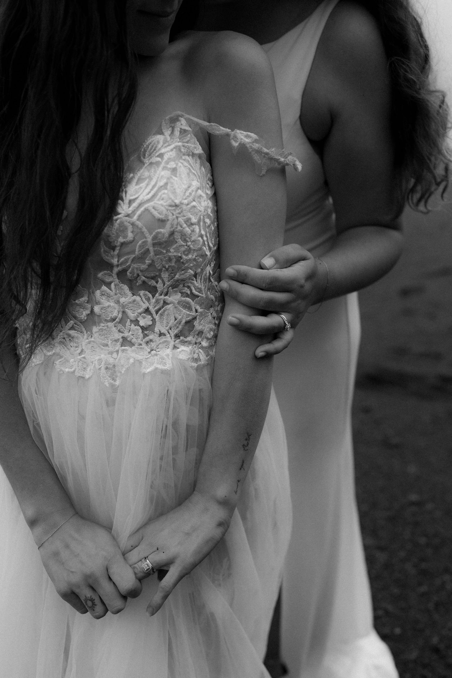 Close up black and white photo of two people holding hands while wearing elegant white wedding dresses.