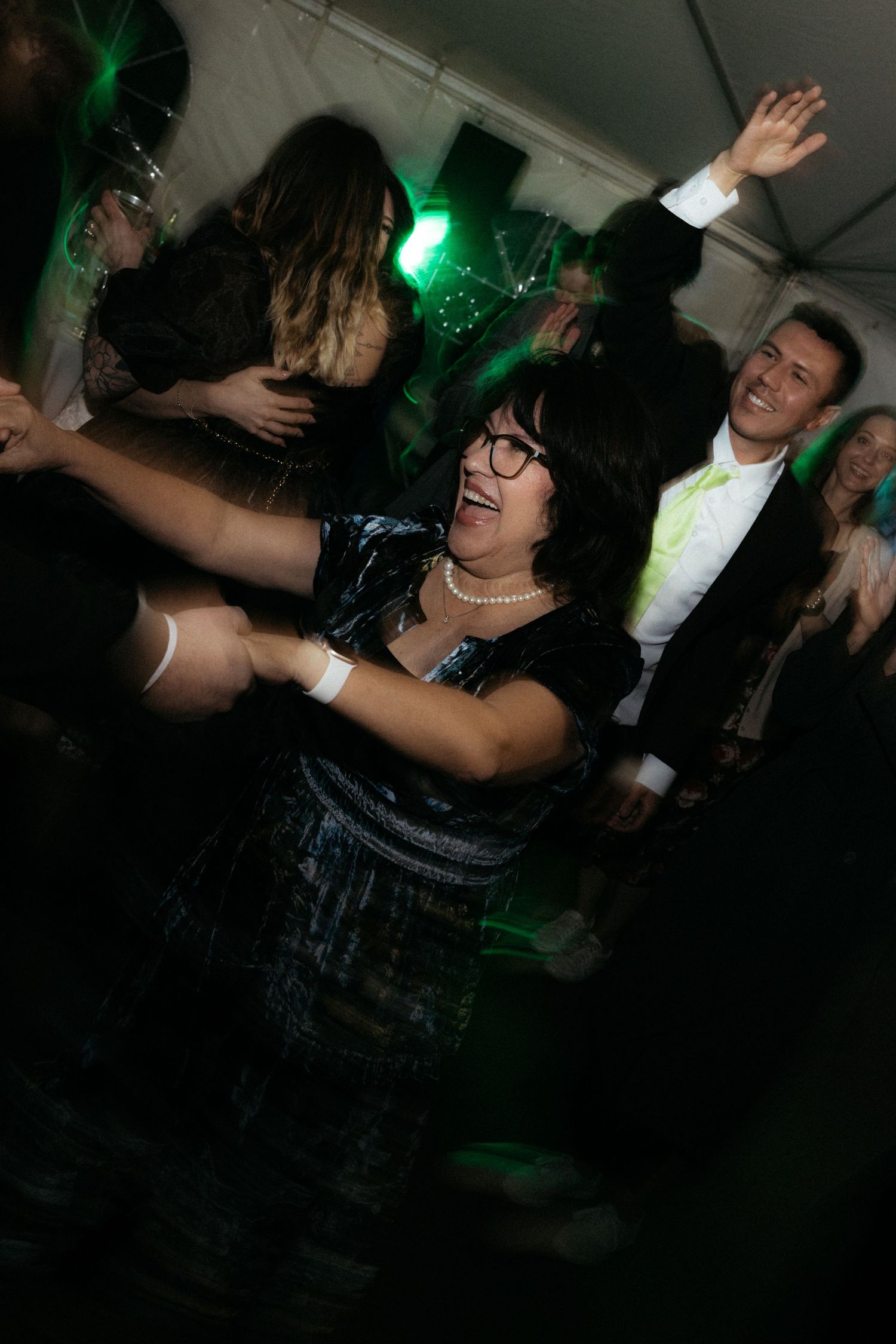 People dancing and celebrating at a nightclub with green lighting effects creating an energetic party atmosphere.