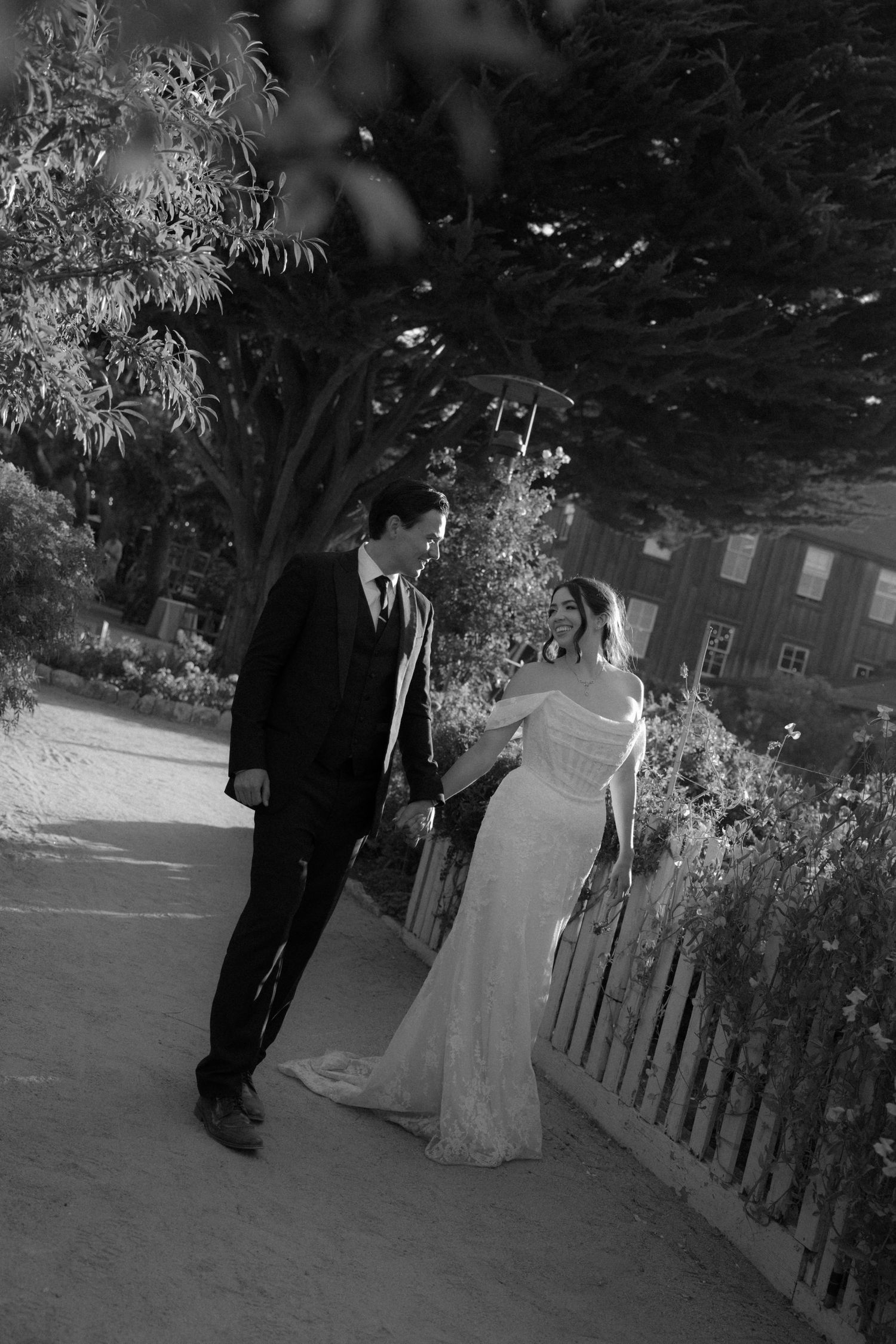 A couple walks together in a garden setting during a wedding photoshoot, captured in black and white.