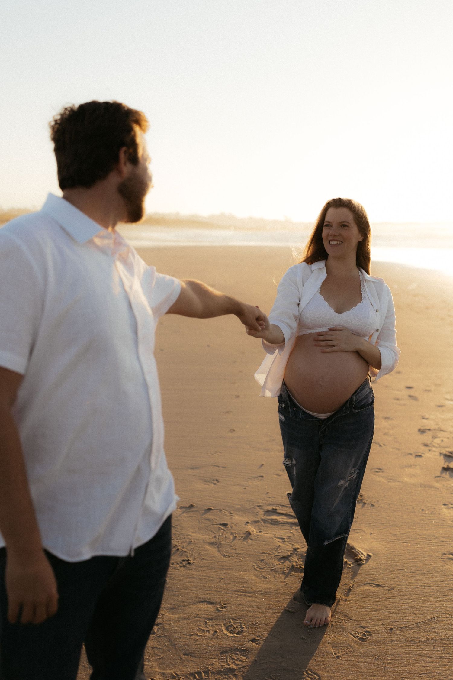 A couple playfully interacts on a sandy beach at sunset, creating a romantic silhouette against the warm light.