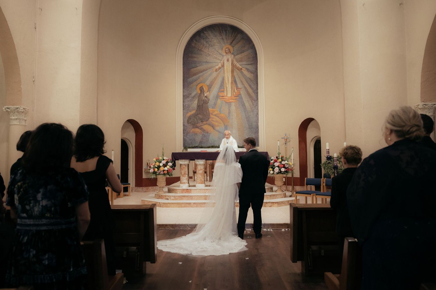 Wide shot of a wedding ceremony in a church with a sunburst mural at the altar.