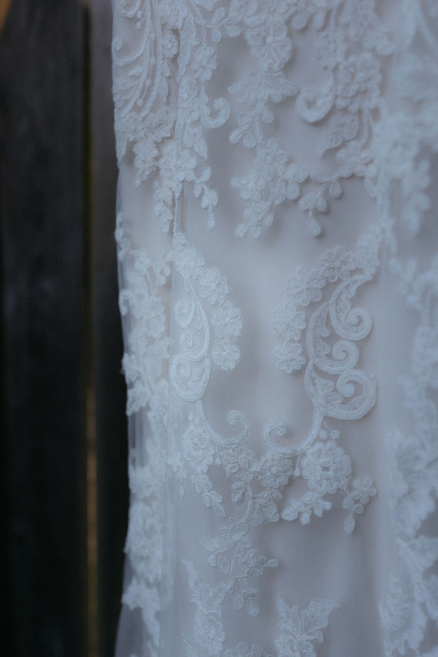 Close-up detail of delicate white lace pattern on wedding dress fabric with intricate floral embroidery.