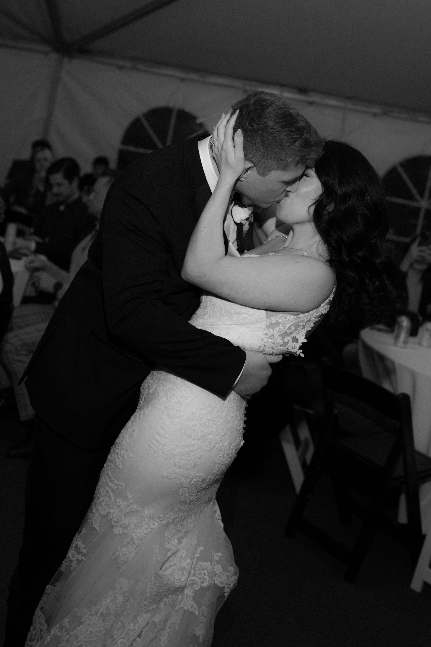 A romantic black and white photo of a couple sharing their first dance at a wedding reception under a tent.