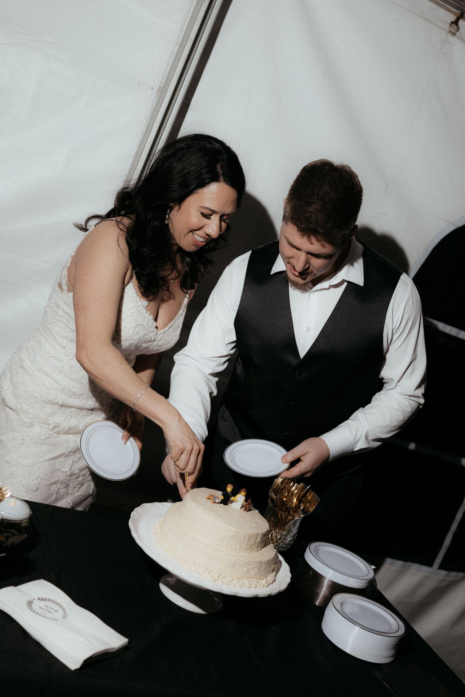 A couple in wedding attire cuts their white wedding cake together during their reception celebration.