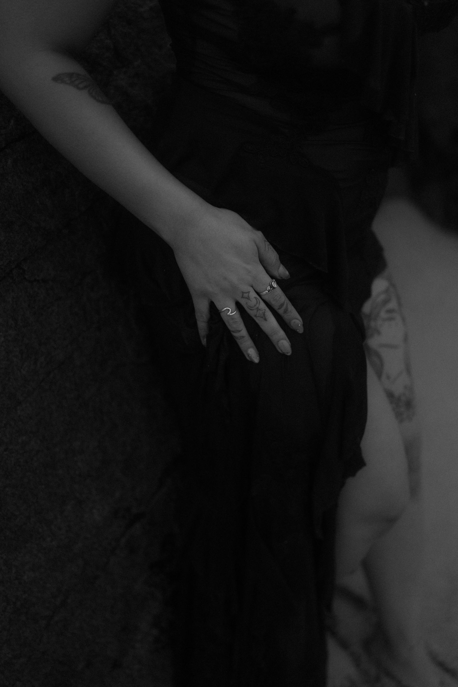 Close-up shot of hands with rings against dark fabric creating an ethereal mood.