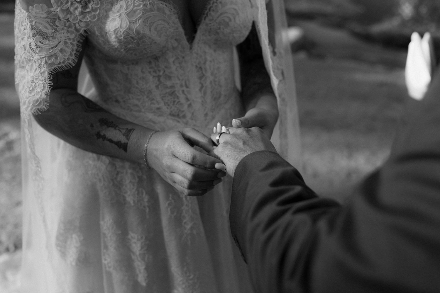 Black and white close-up of groom placing wedding ring on brides tattooed hand.