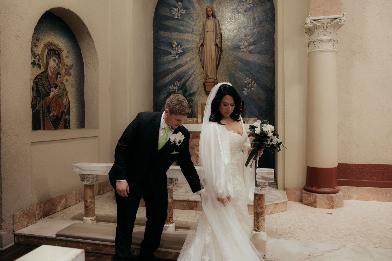 Religious murals and artwork decorate the walls of a church altar area during a wedding ceremony.