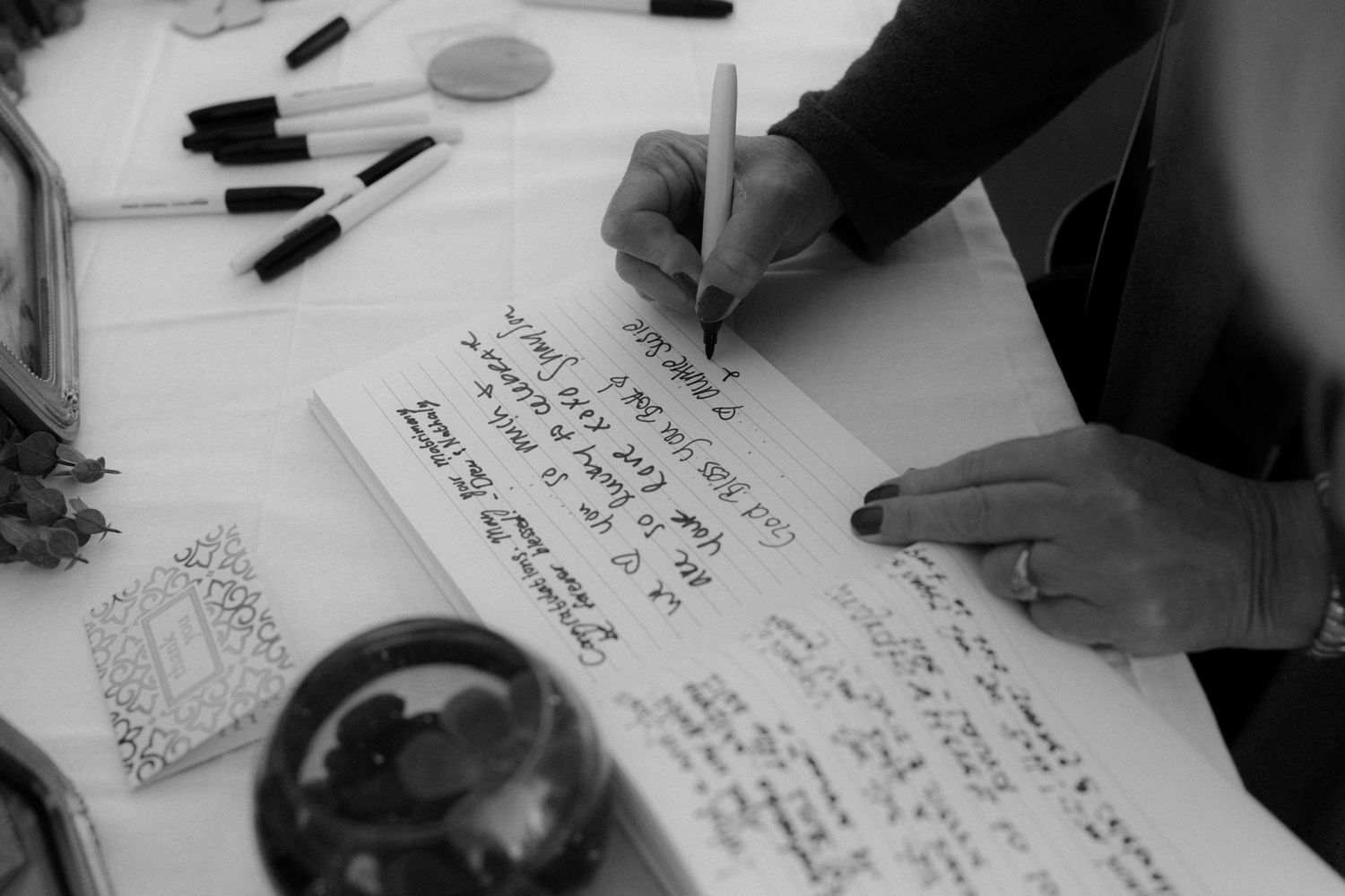 Black and white image of guests writing messages in a wedding guestbook.