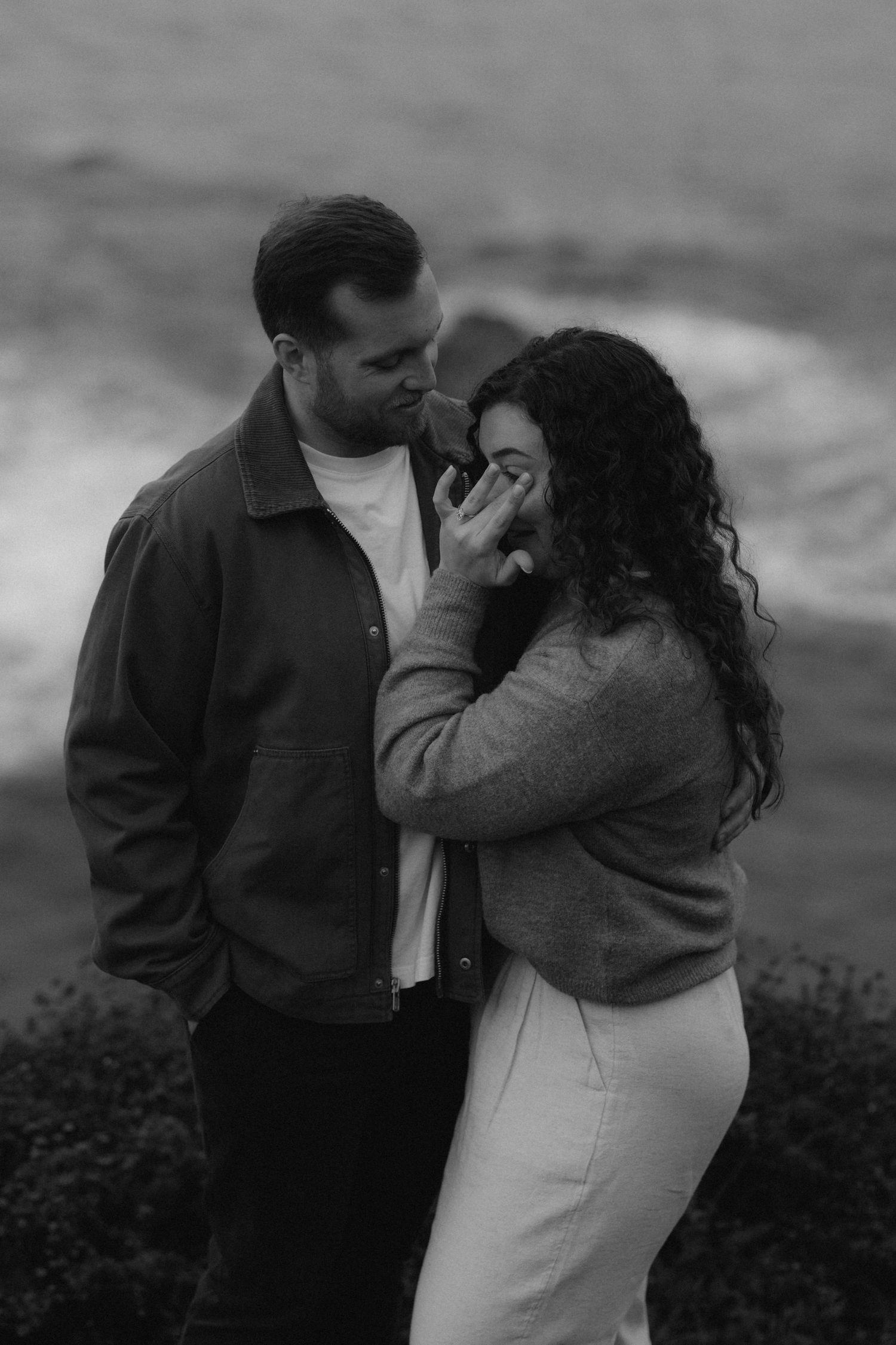 Intimate moment captured against moody coastal backdrop during sunset.