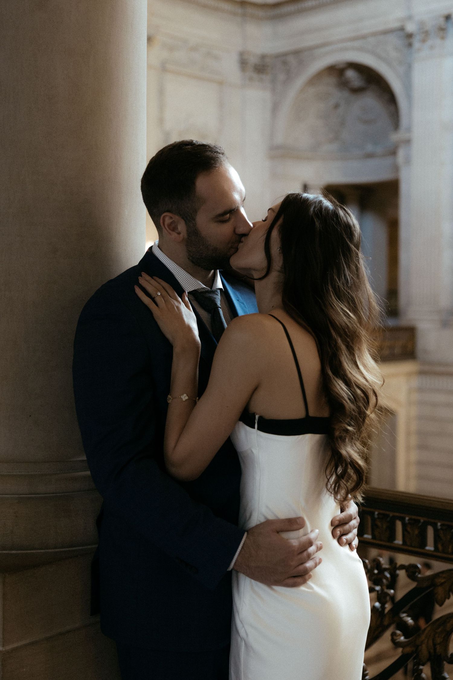 A romantic moment unfolds between a couple in formal attire within a grand marble-columned interior.