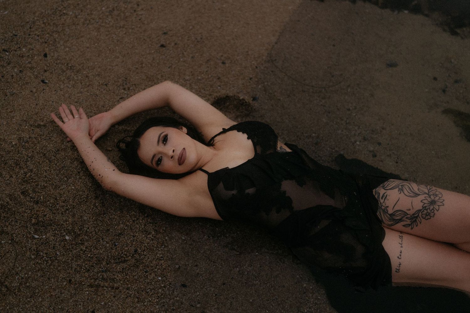 Artistic black and white photo of a figure lying on sand wearing dark clothing.