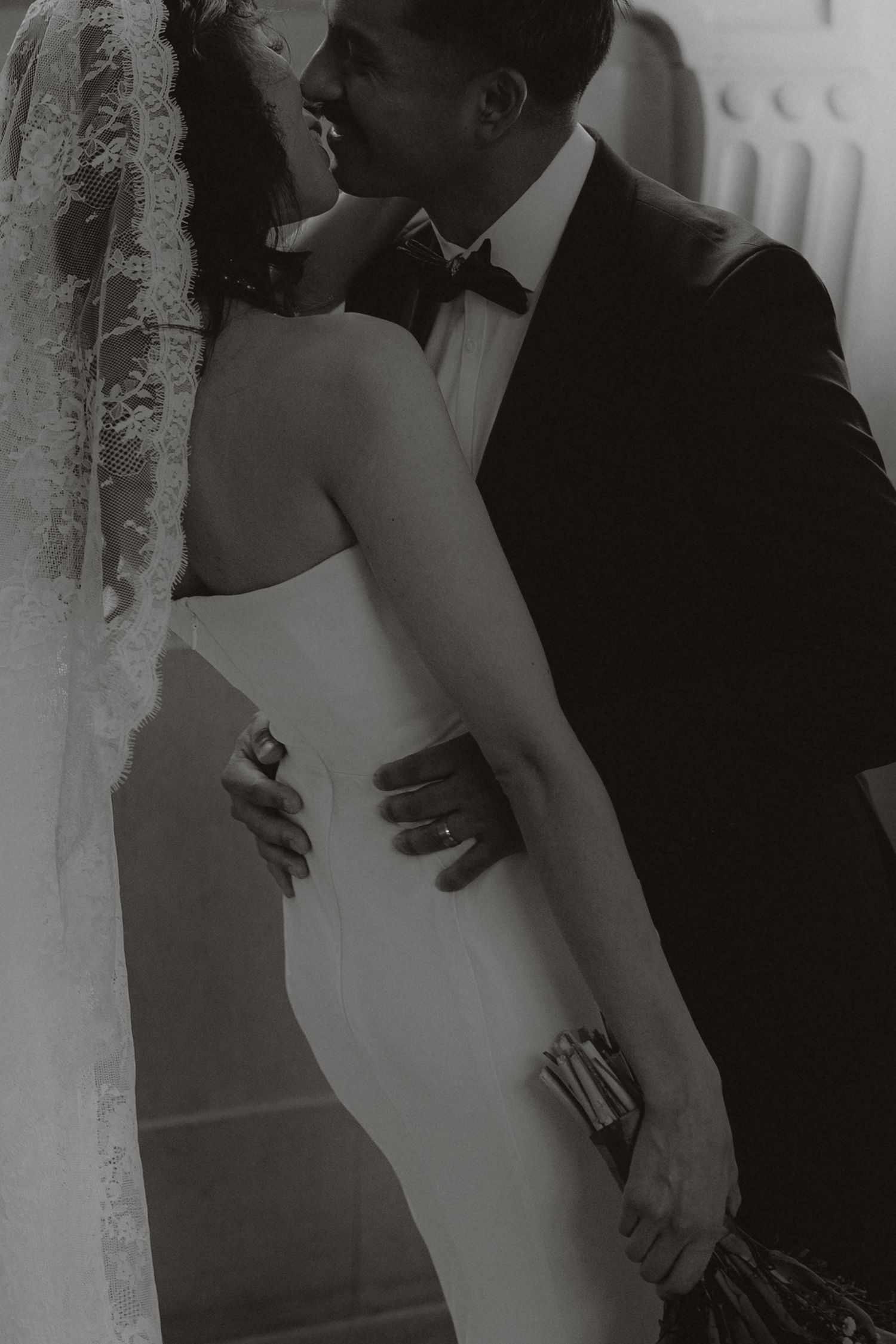 An intimate black and white portrait of newlyweds embracing in formal wedding attire.