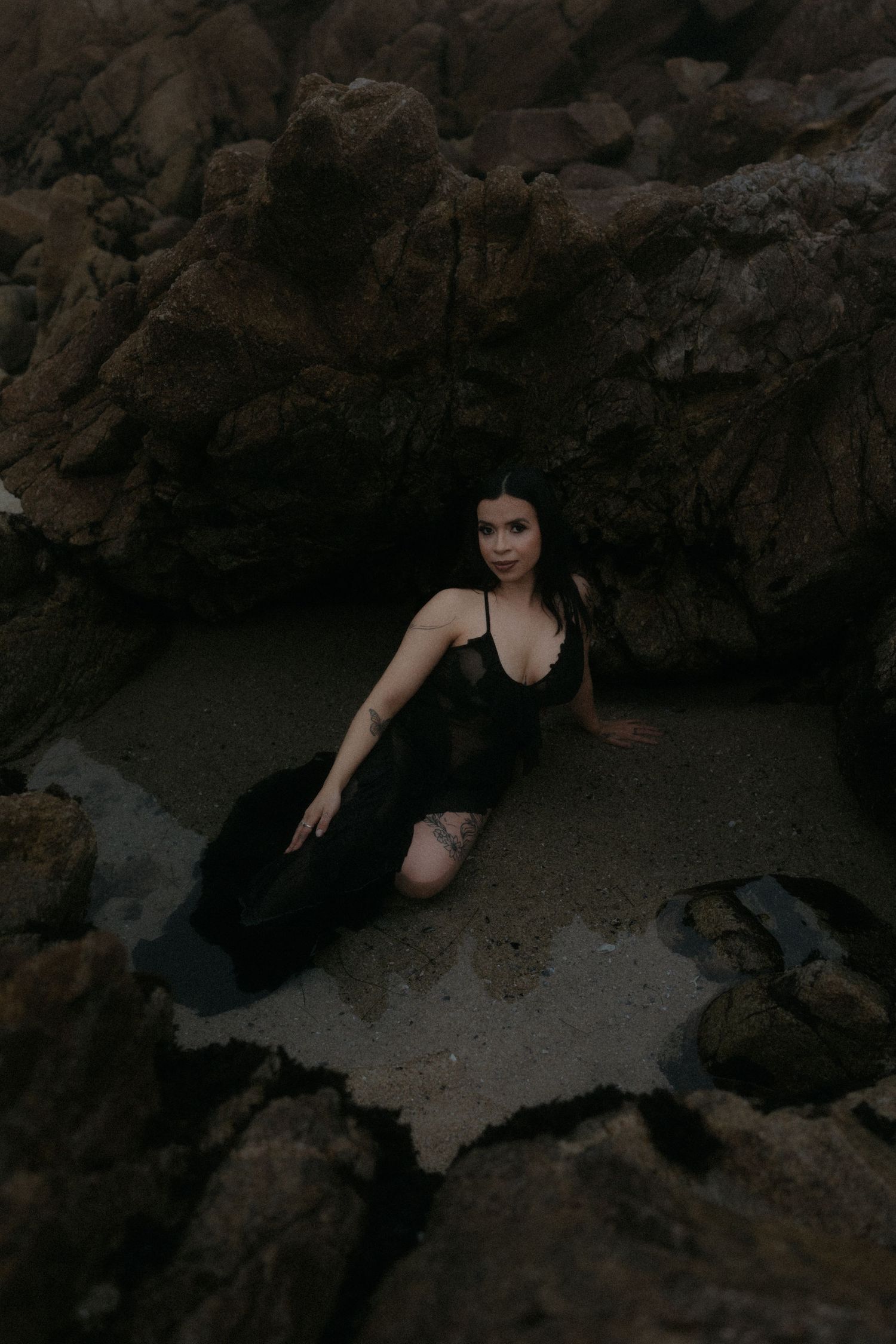 Dramatic pose among dark rocky coastal formations at dusk.