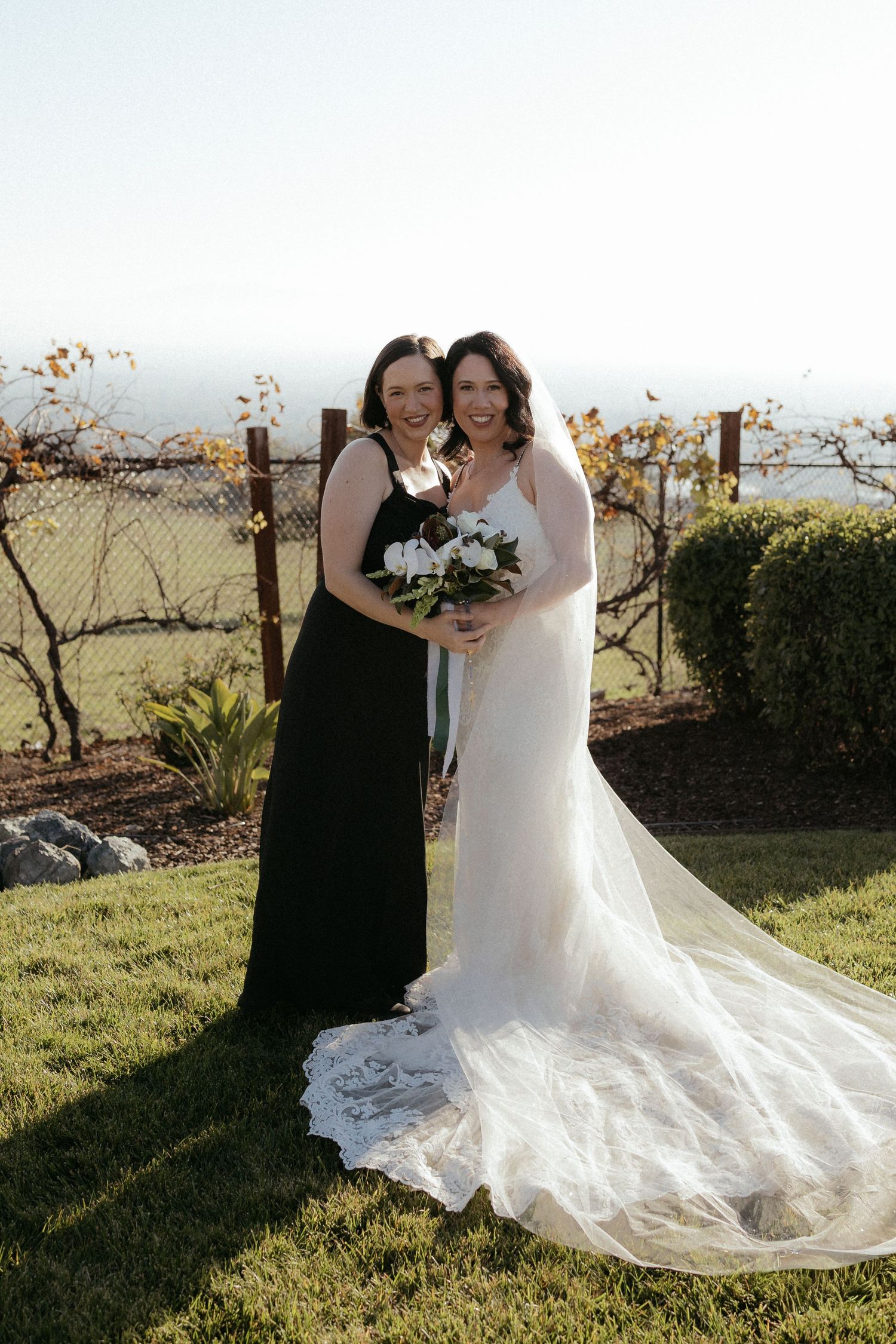 Two people in wedding attire pose together in an outdoor garden setting with scenic views.