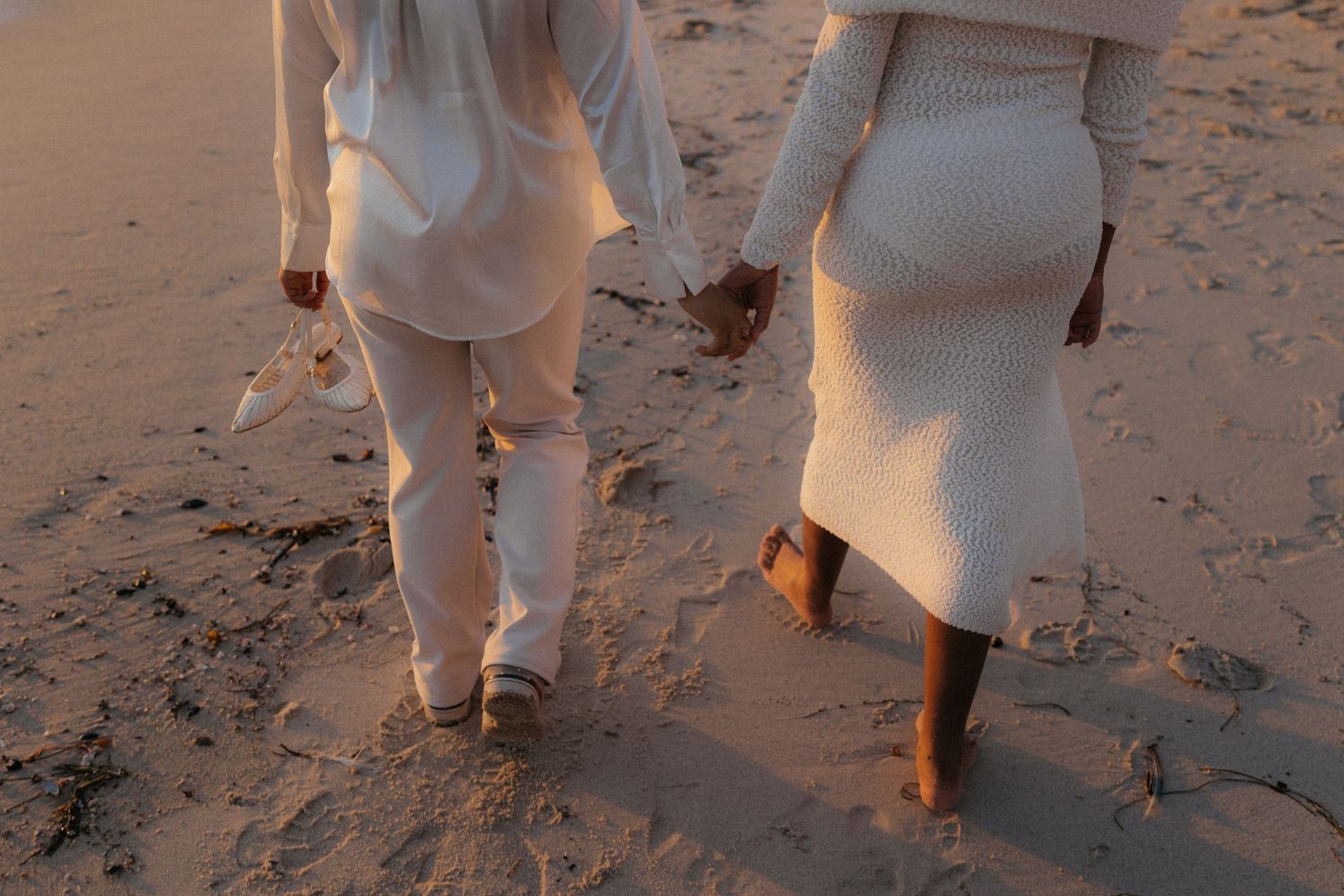 A group of people in white clothing walking along a sandy beach at sunset.