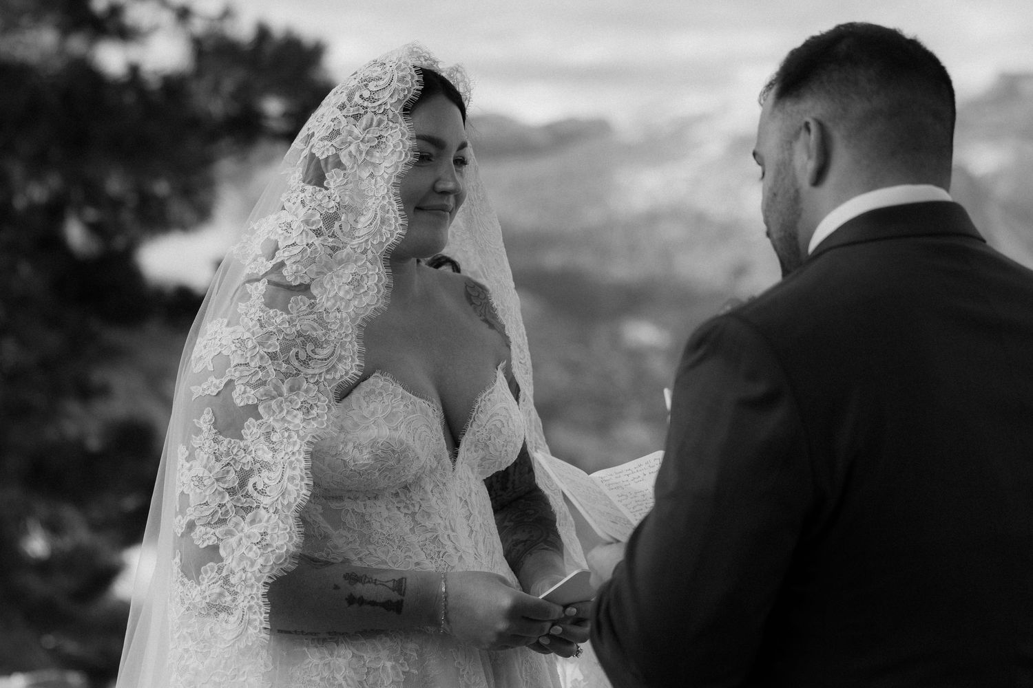 Black and white photo of bride and groom holding hands during outdoor ceremony.
