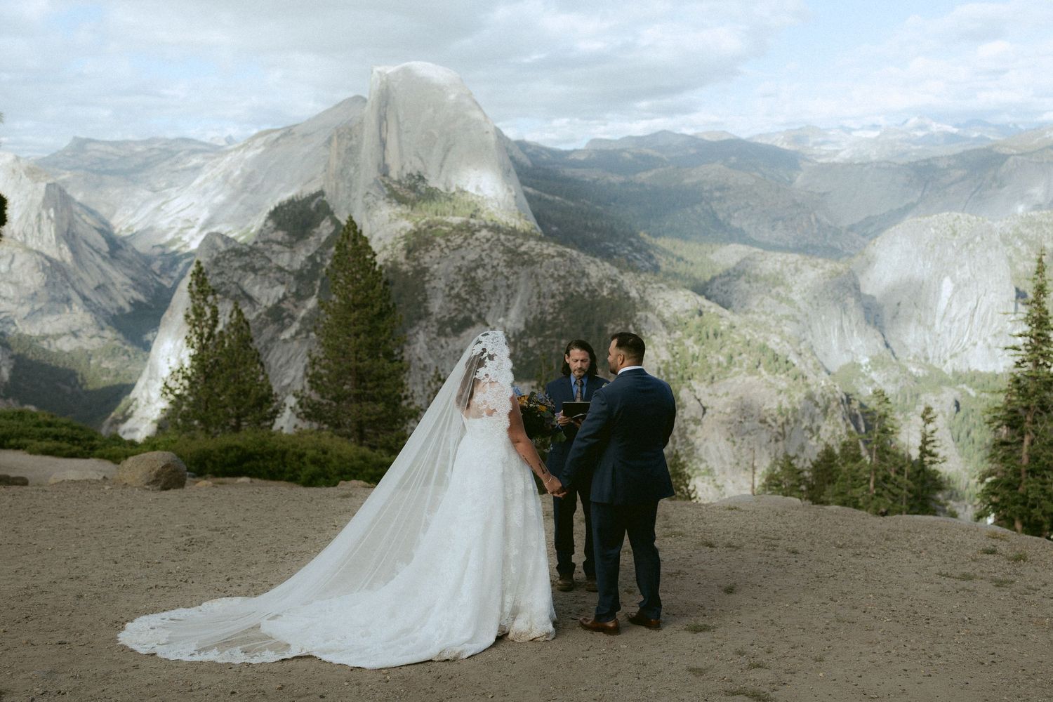 Couple exchanges vows at Glacier Point Yosemite with Half Dome mountain backdrop during outdoor elopement ceremony.