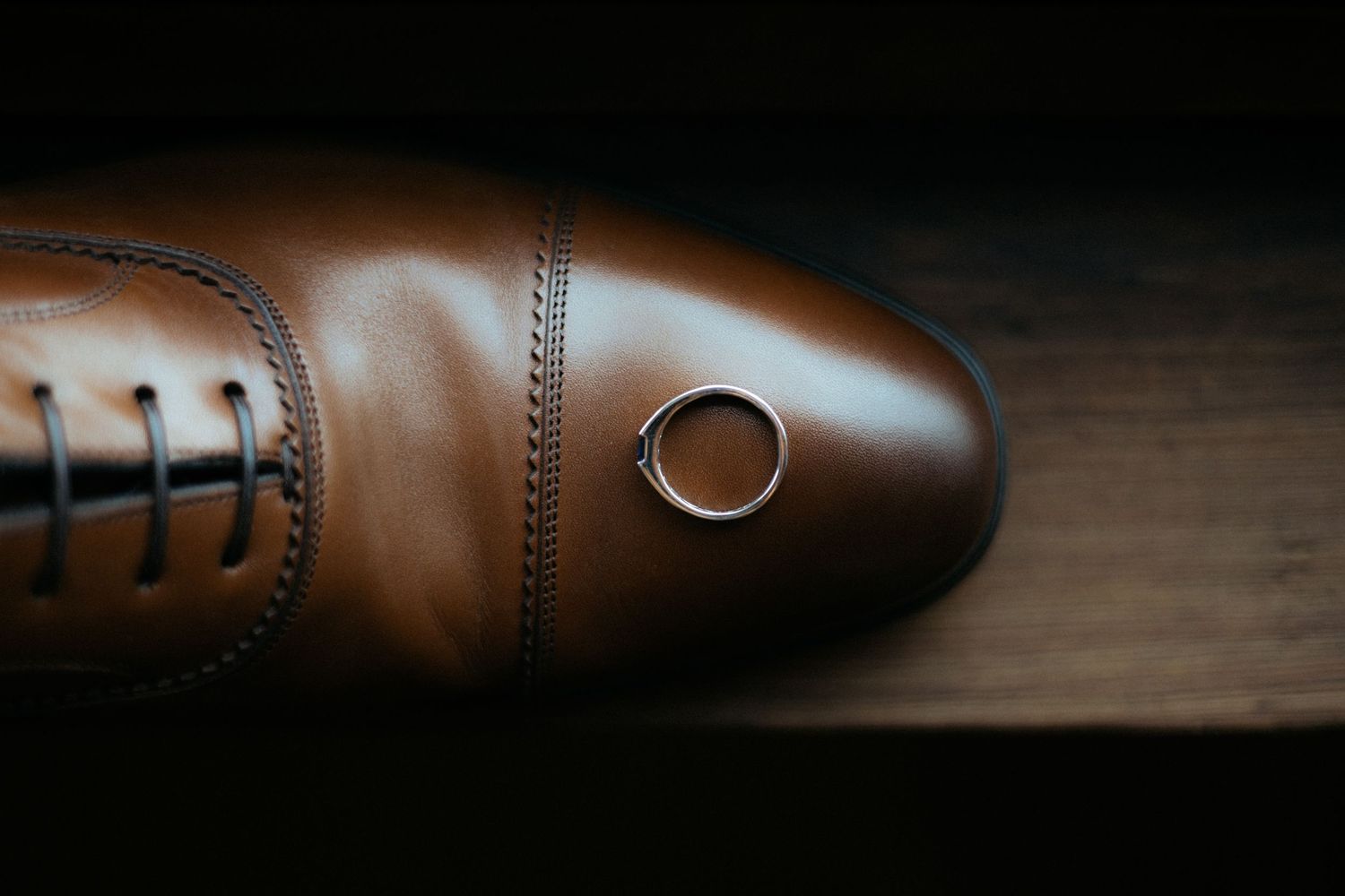 Wedding ring placed artistically on a brown leather dress shoe.