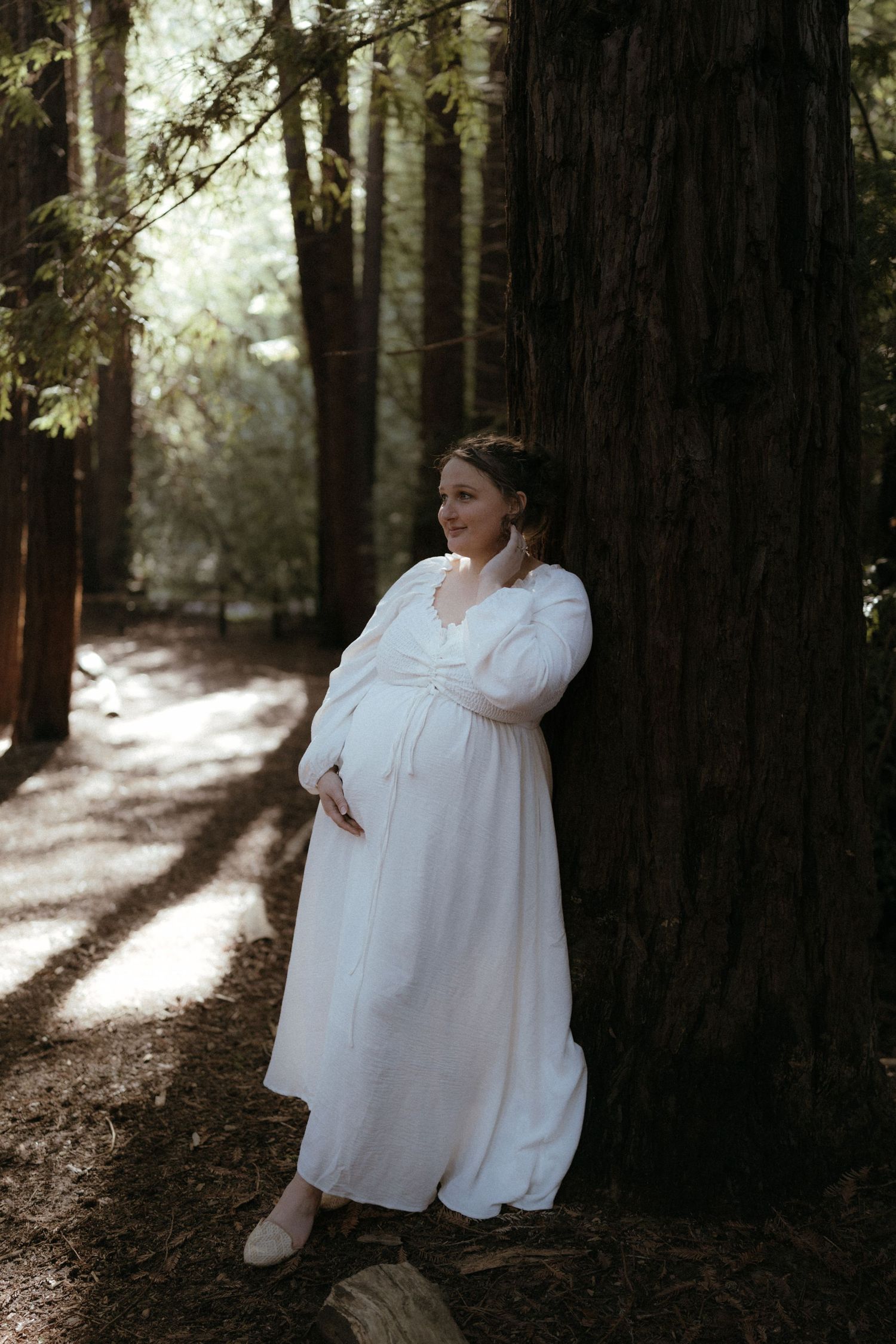 Ethereal forest photoshoot featuring figures in flowing white dresses embracing among tall redwood trees in dappled sunlight.