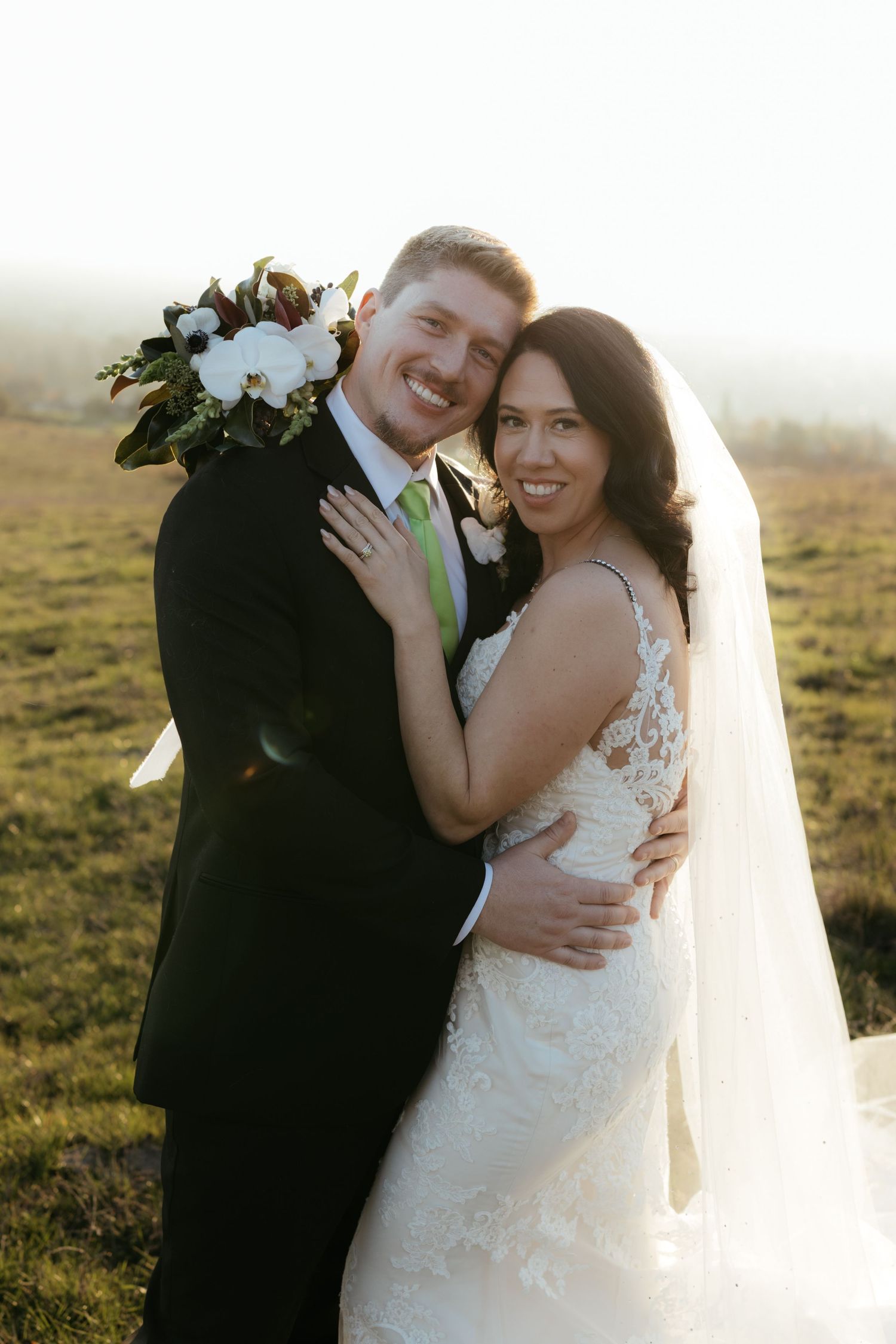 Newlyweds embrace and laugh together in a sunlit field during golden hour wedding photos.