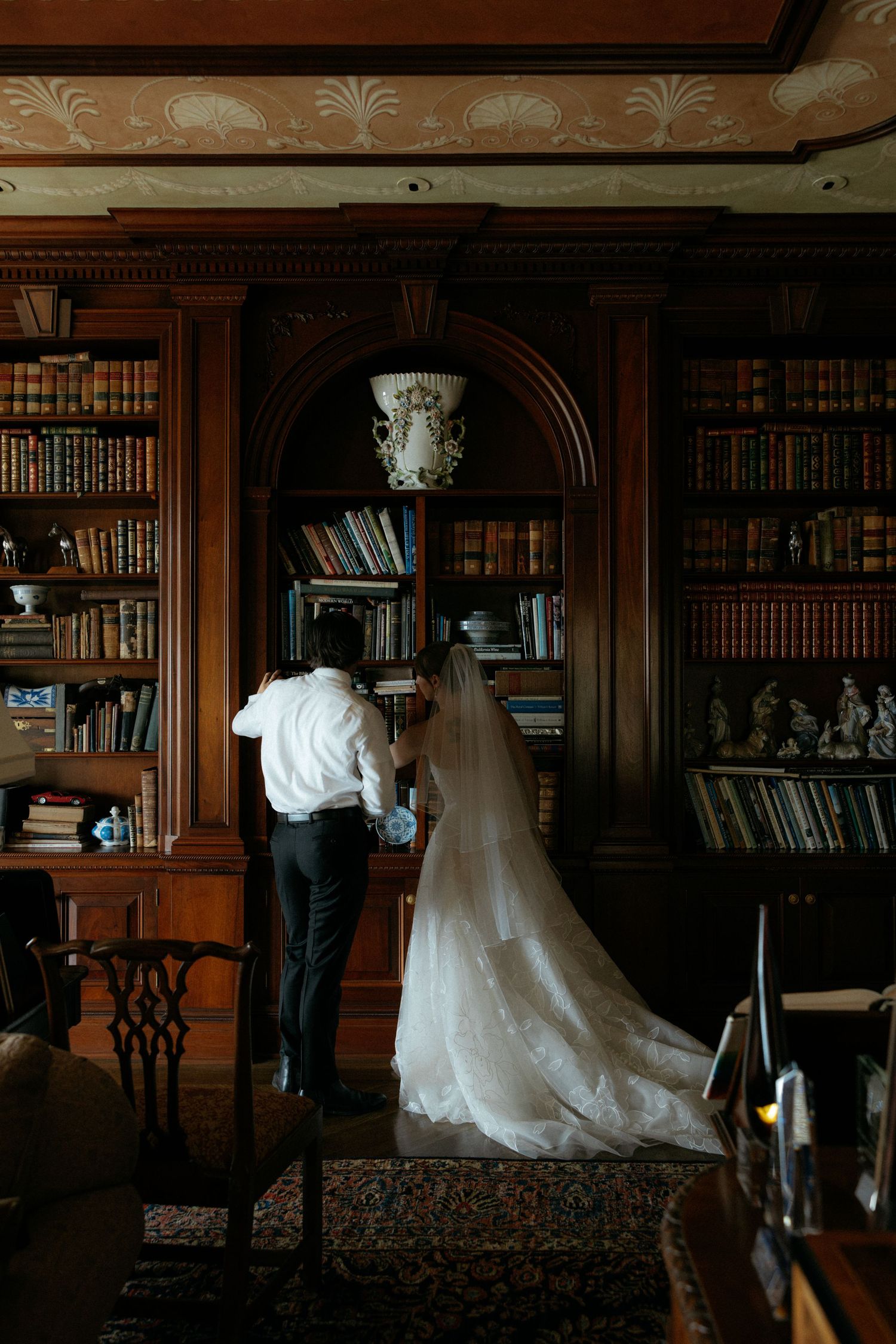 Bride and groom share an intimate moment browsing books in an elegant wood-paneled library on their wedding day.