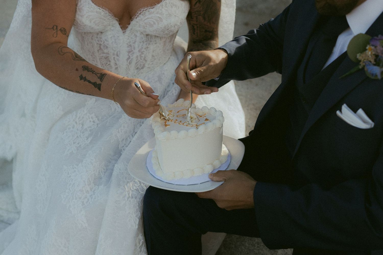 Close-up of tattooed bride and groom cutting white heart-shaped wedding cake.