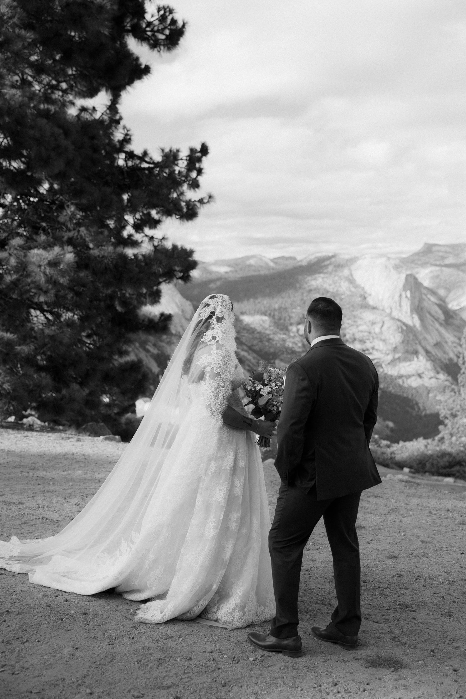 Black and white photo of bride and groom admiring scenic mountain valley views at Yosemite.