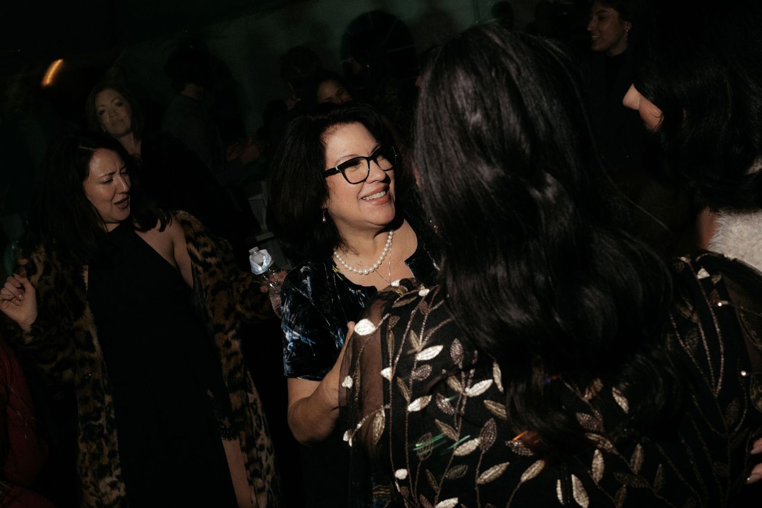 Crowd of people dancing and moving in a dark nightclub setting.