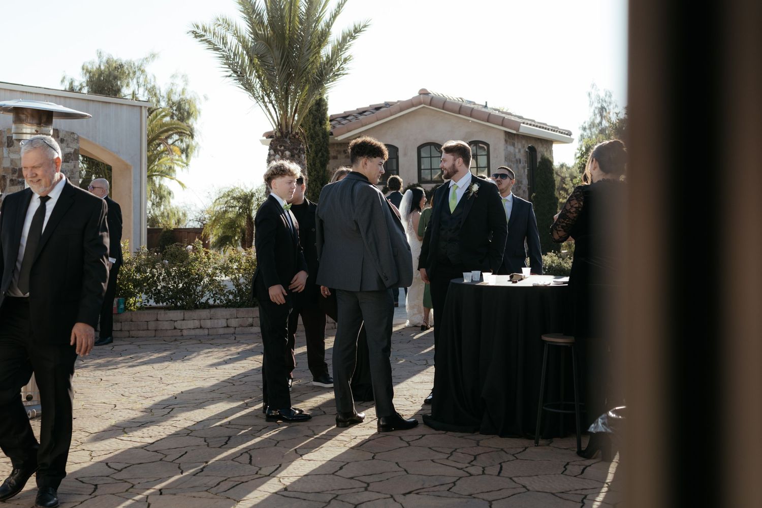 Outdoor wedding gathering at a venue with palm trees and Spanish-style architecture in the background.