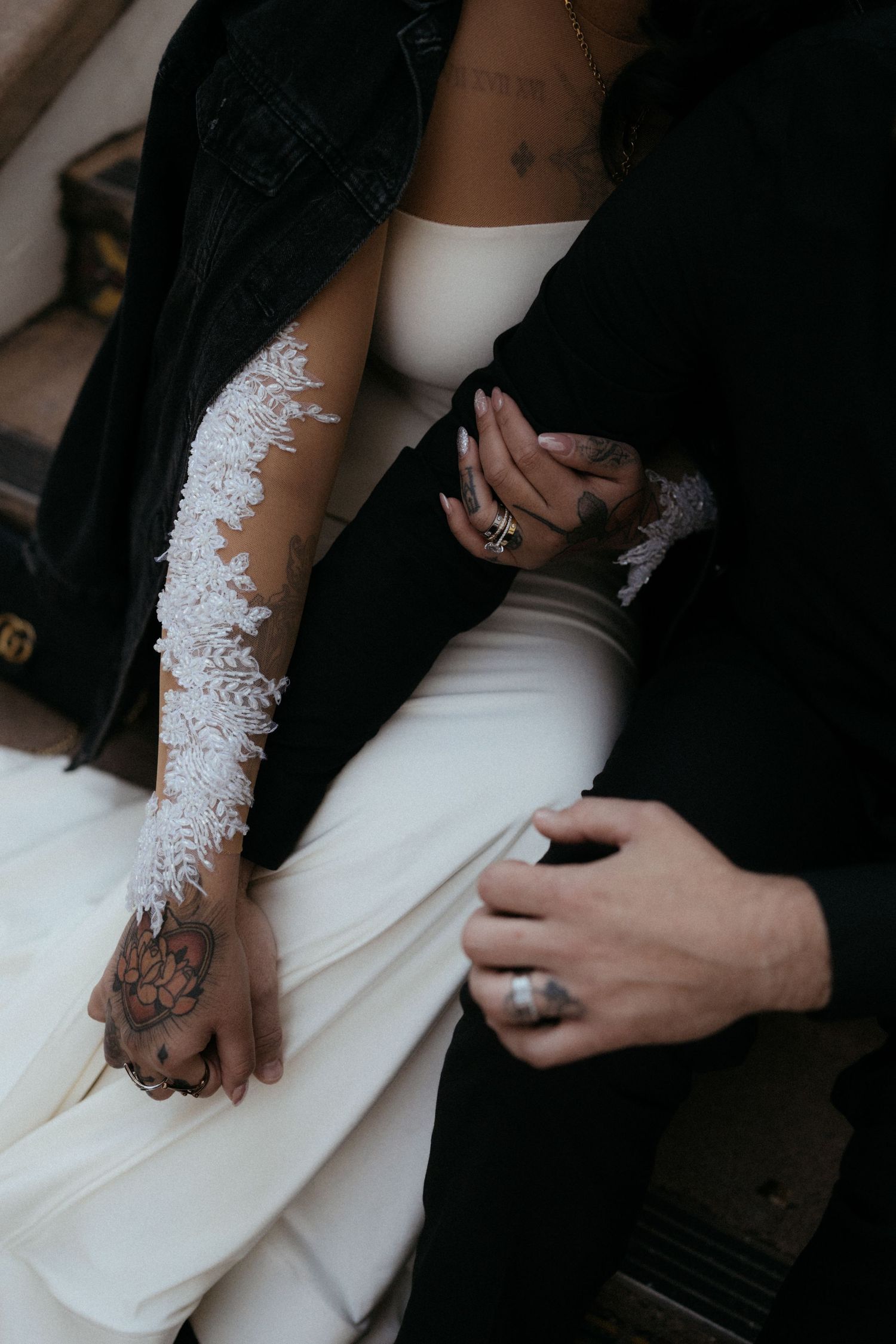 Close-up view of hands wearing black and white attire with lace details and jewelry against dark background.