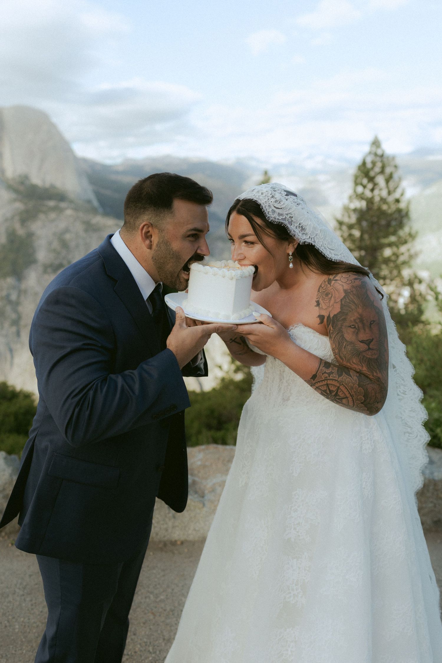 Bride and groom sharing a bite of white wedding cake with mountain backdrop at Yosemite.