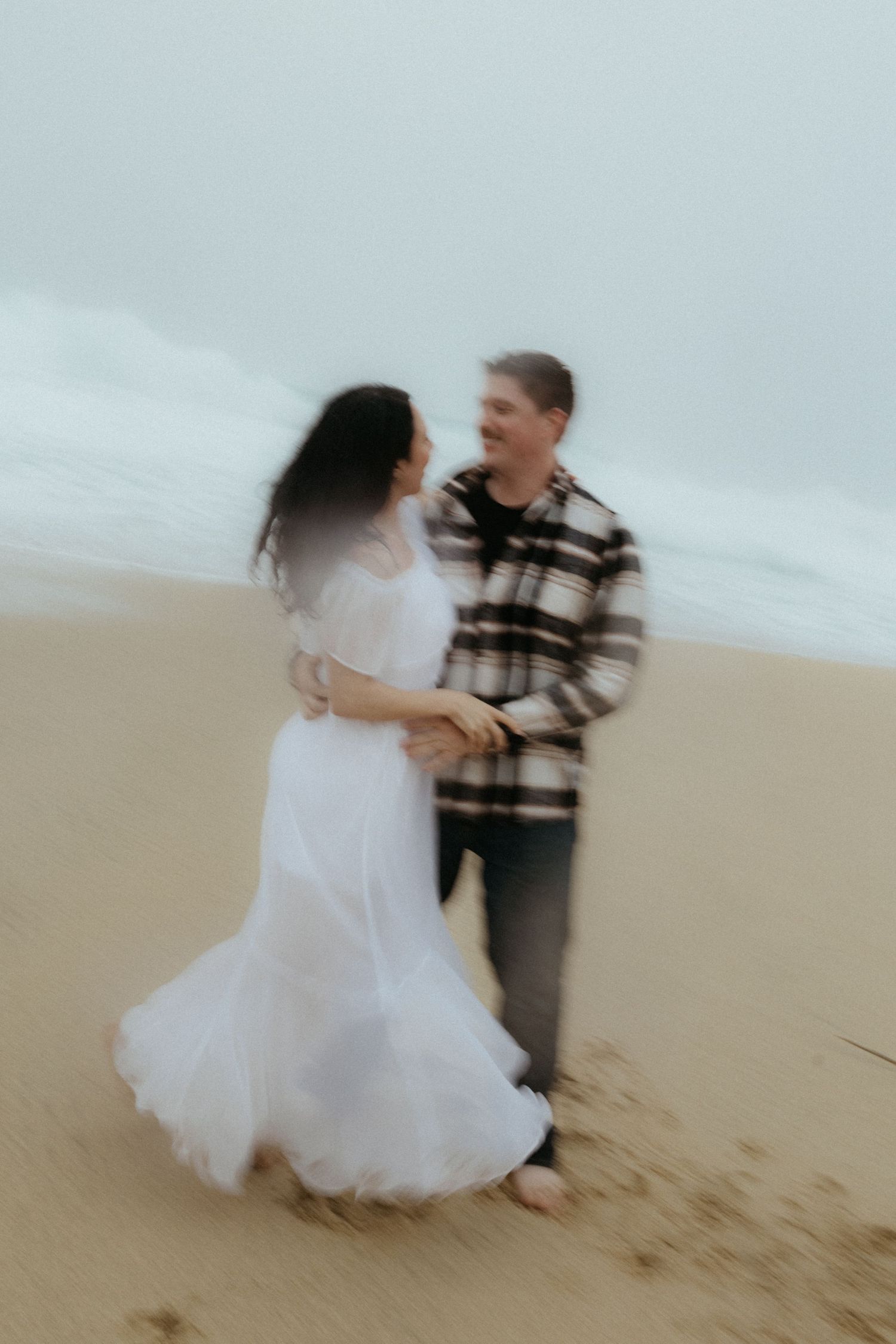 A couple dances and spins on the beach creating movement in their formal attire.