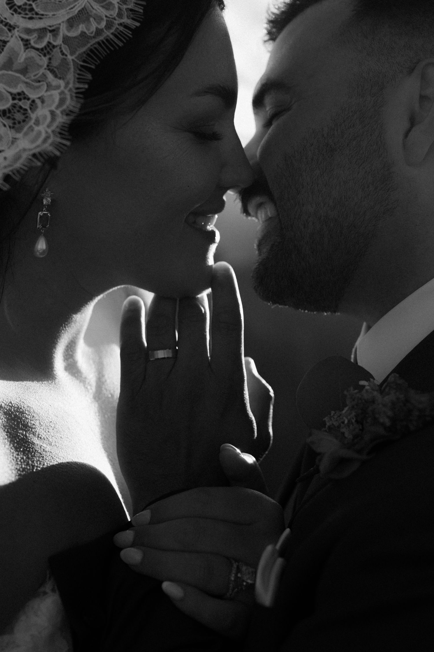 Black and white wedding photo of bride and groom sharing an intimate moment, hands touching faces before a kiss.