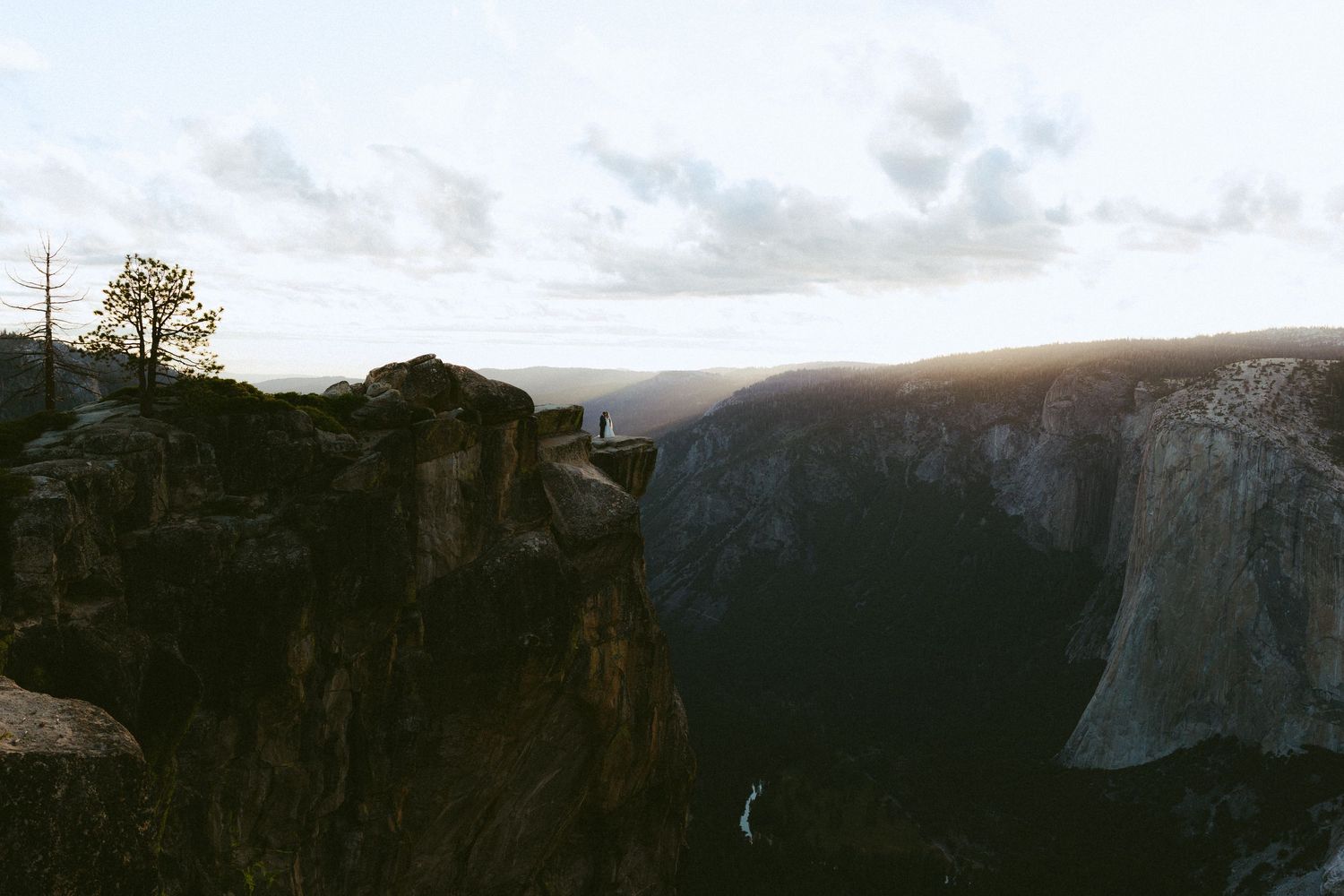 Dramatic canyon view at sunset in Yosemite with rocky cliffs and a lone figure standing on the edge.