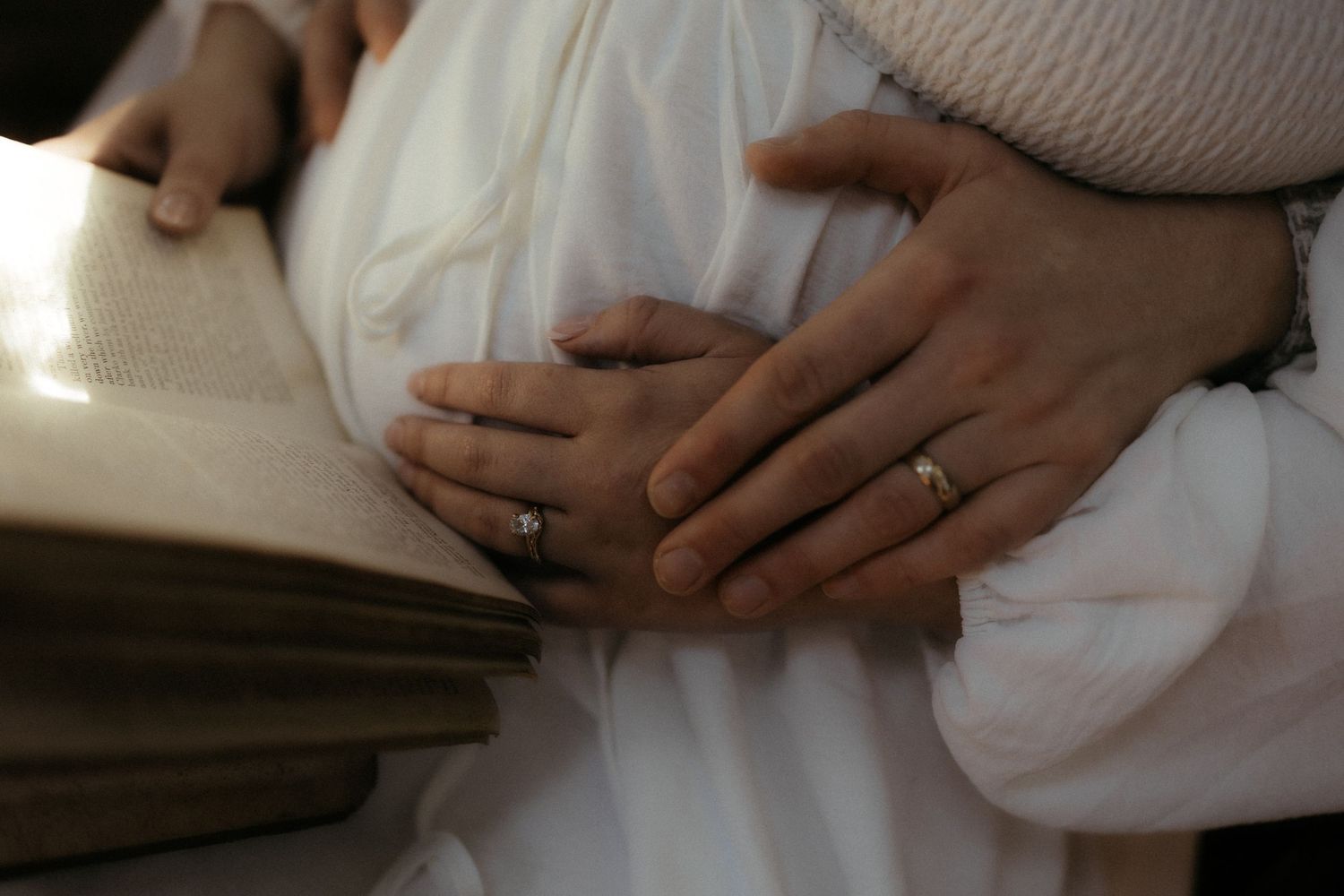 Close-up shot of hands with wedding rings resting against white fabric.