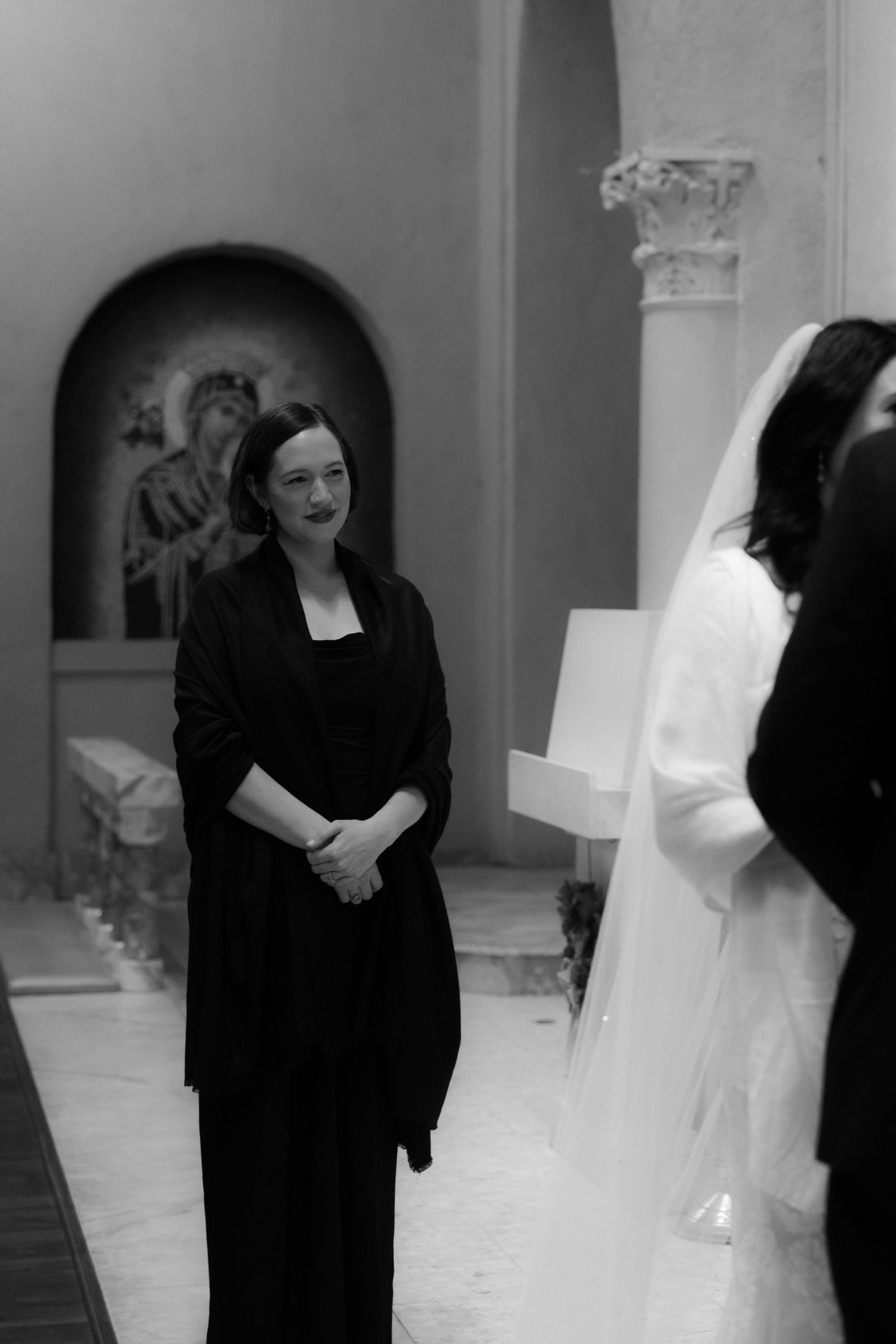 A woman in black attire stands in a church during a ceremony.